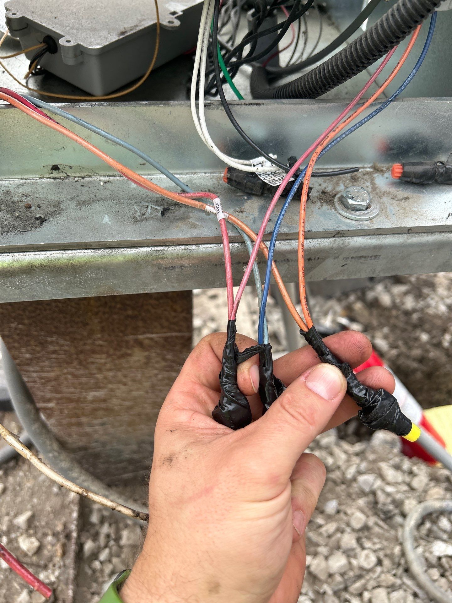 Hand holding several wires with electrical tape, near machinery and other wires.