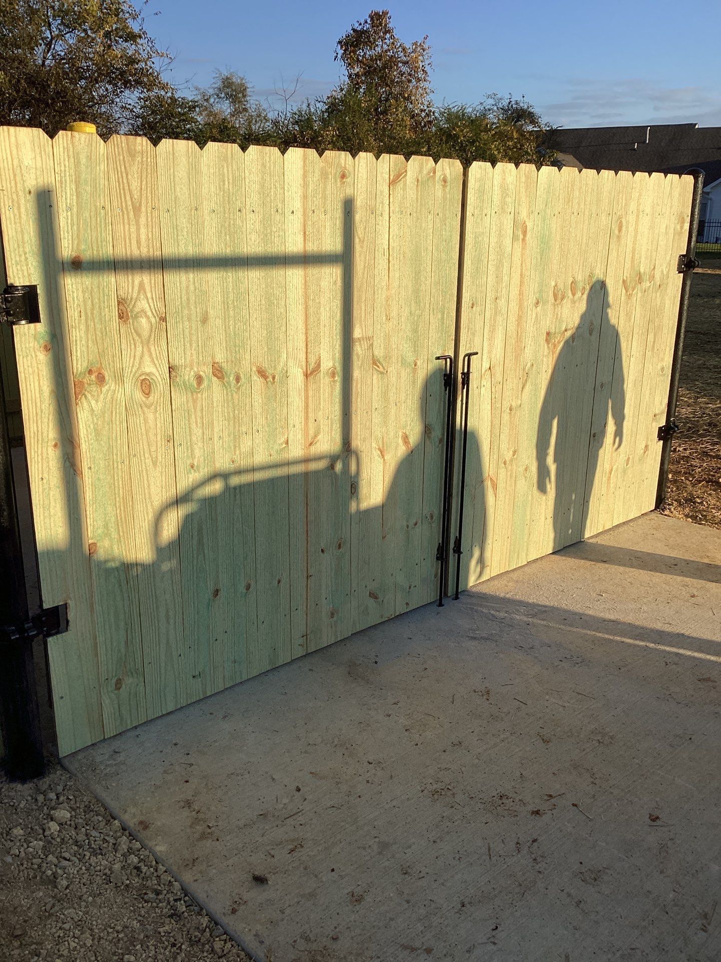 Wooden fence with shadows from a ladder and person on a concrete surface.