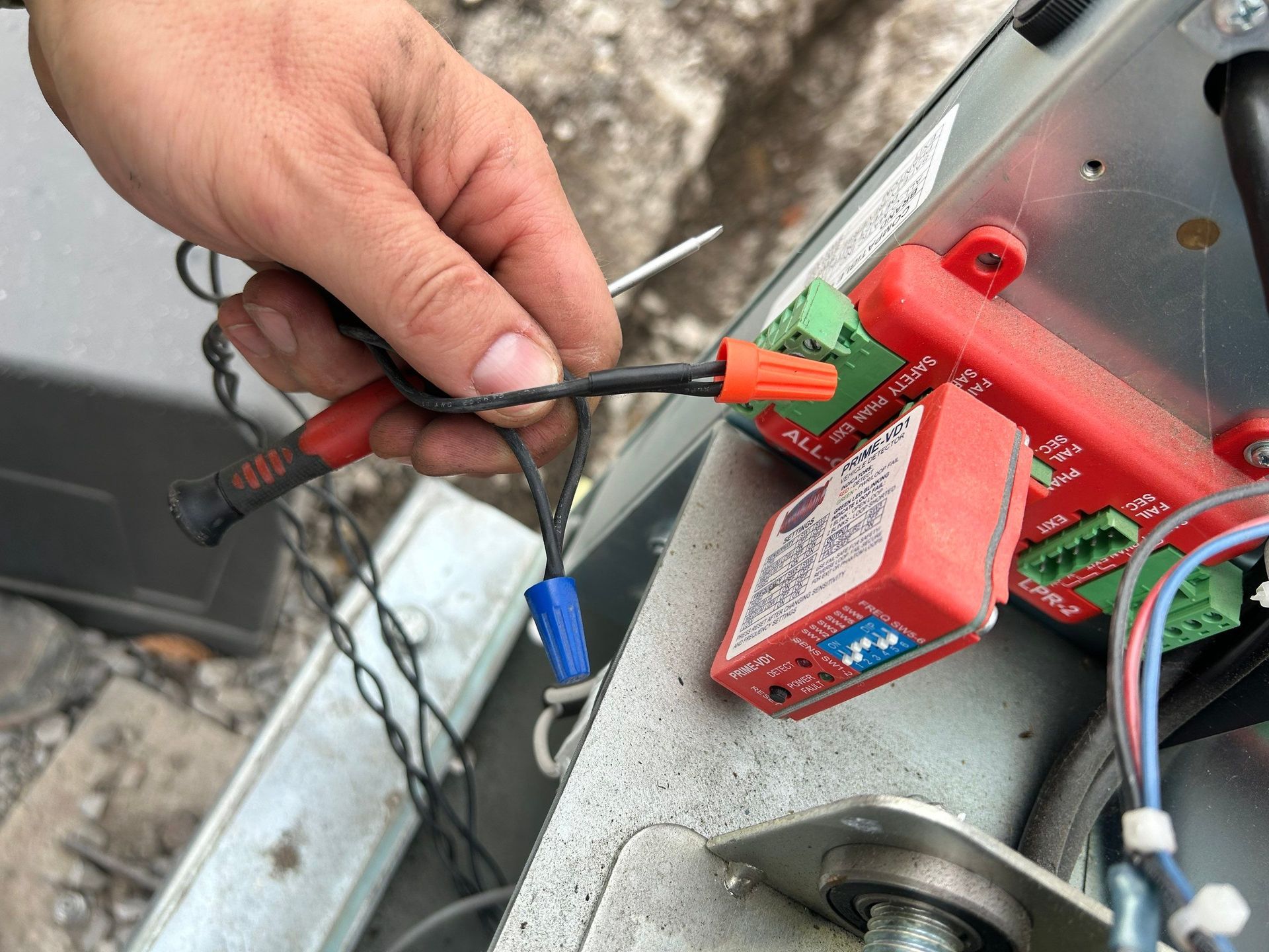 Person wiring electrical components inside a garage door opener. Black and blue wires with wire nuts and a red module.