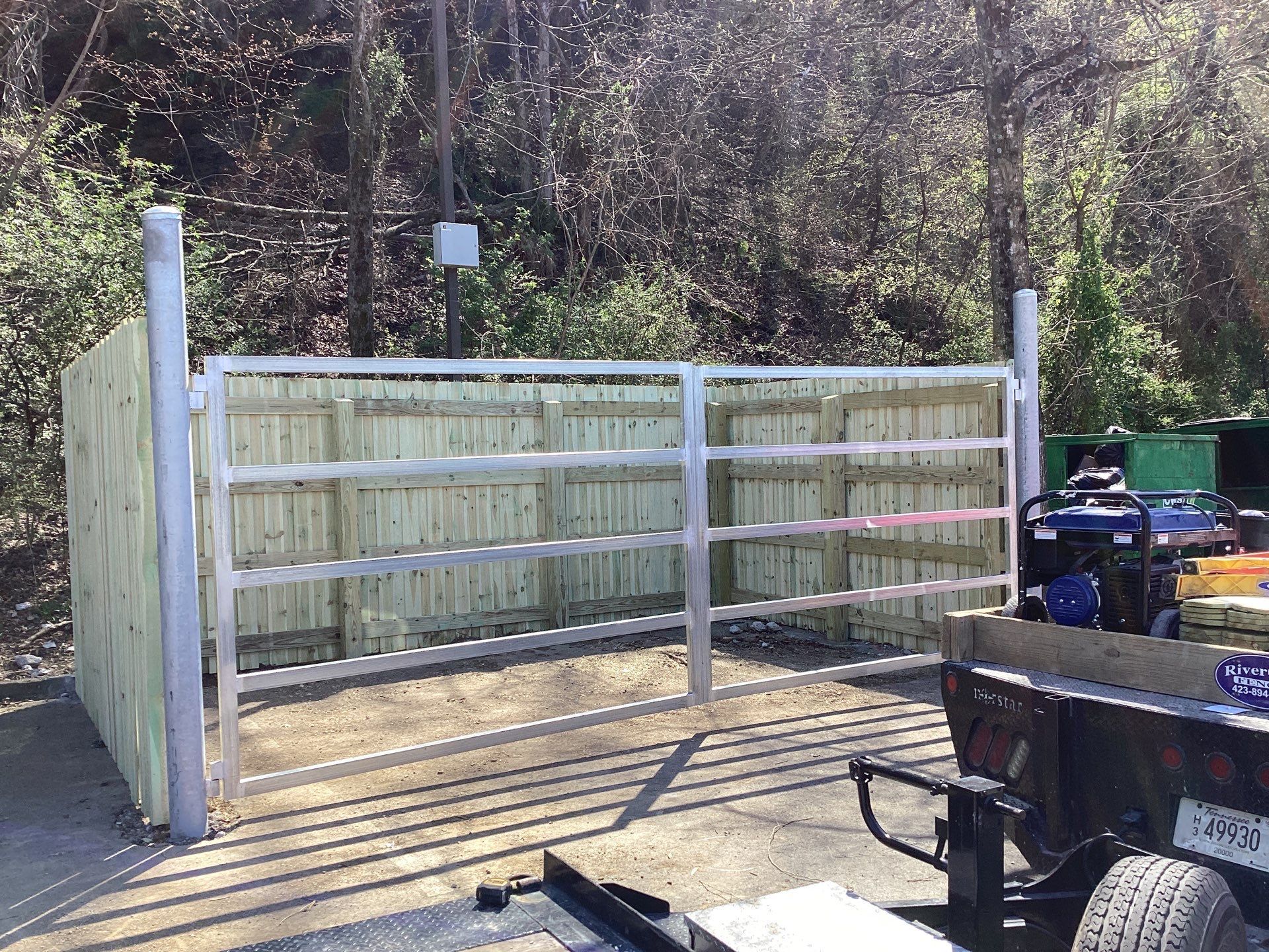 Metal gate and wooden fence on a concrete pad, with trees in the background.