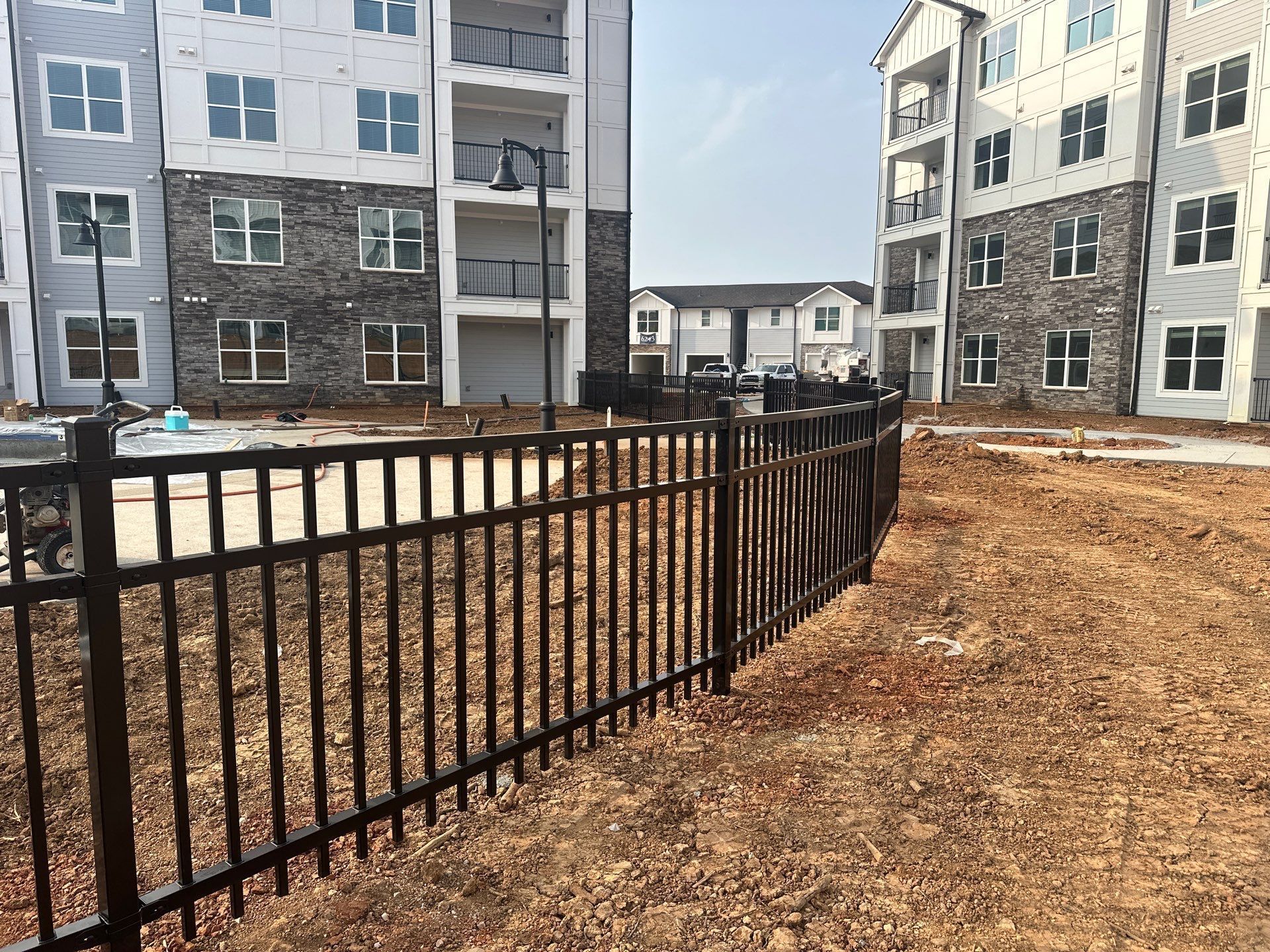 Black metal fence in front of apartment buildings under construction. Brown earth.