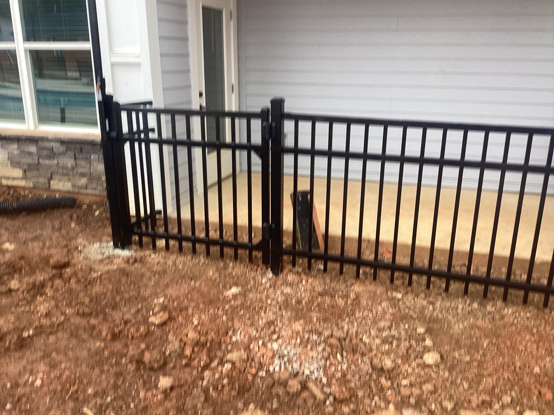 Black metal fence with a gate, in front of a house.