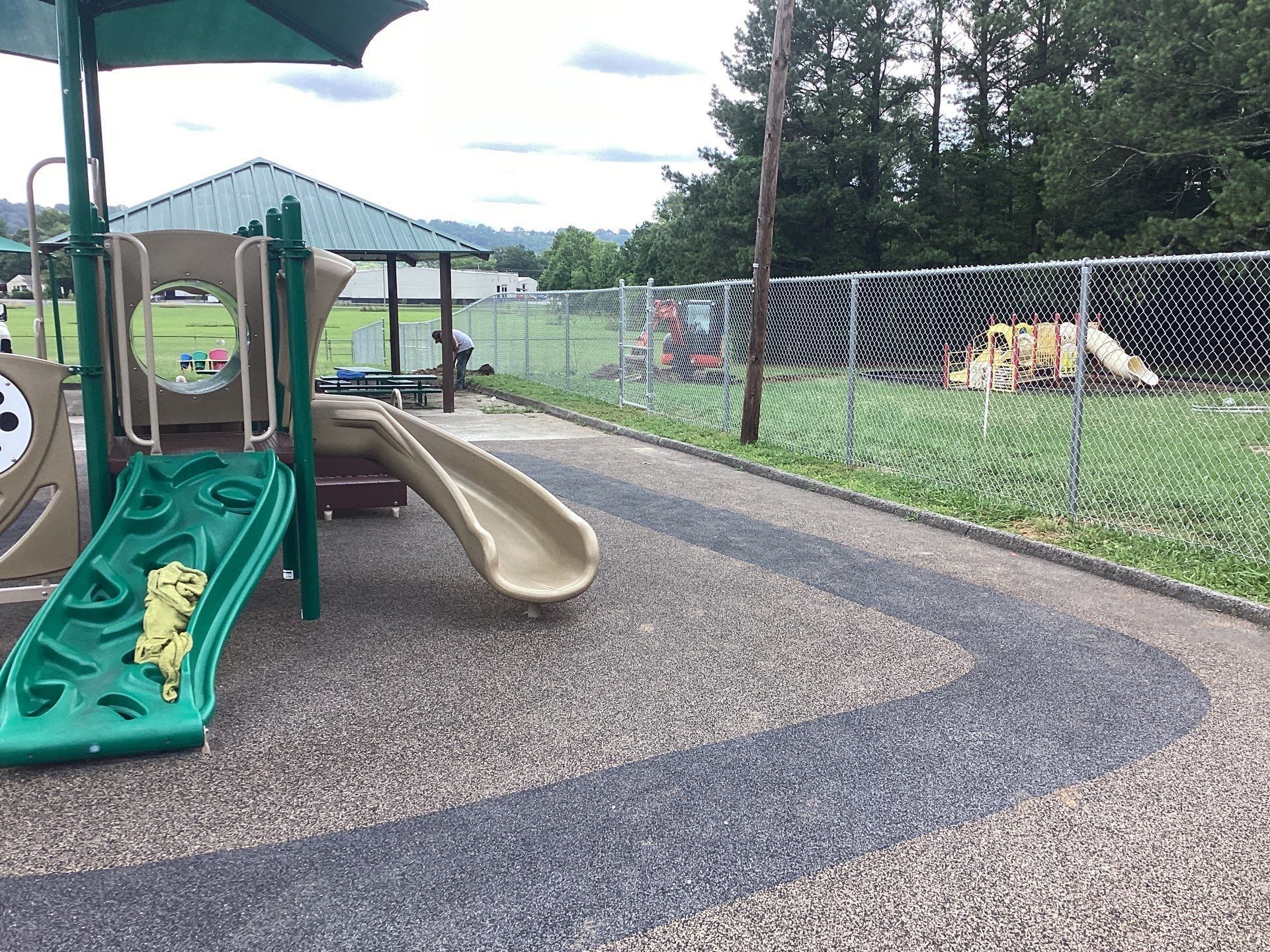 Playground with slides, surrounded by a chain-link fence, on a cloudy day.