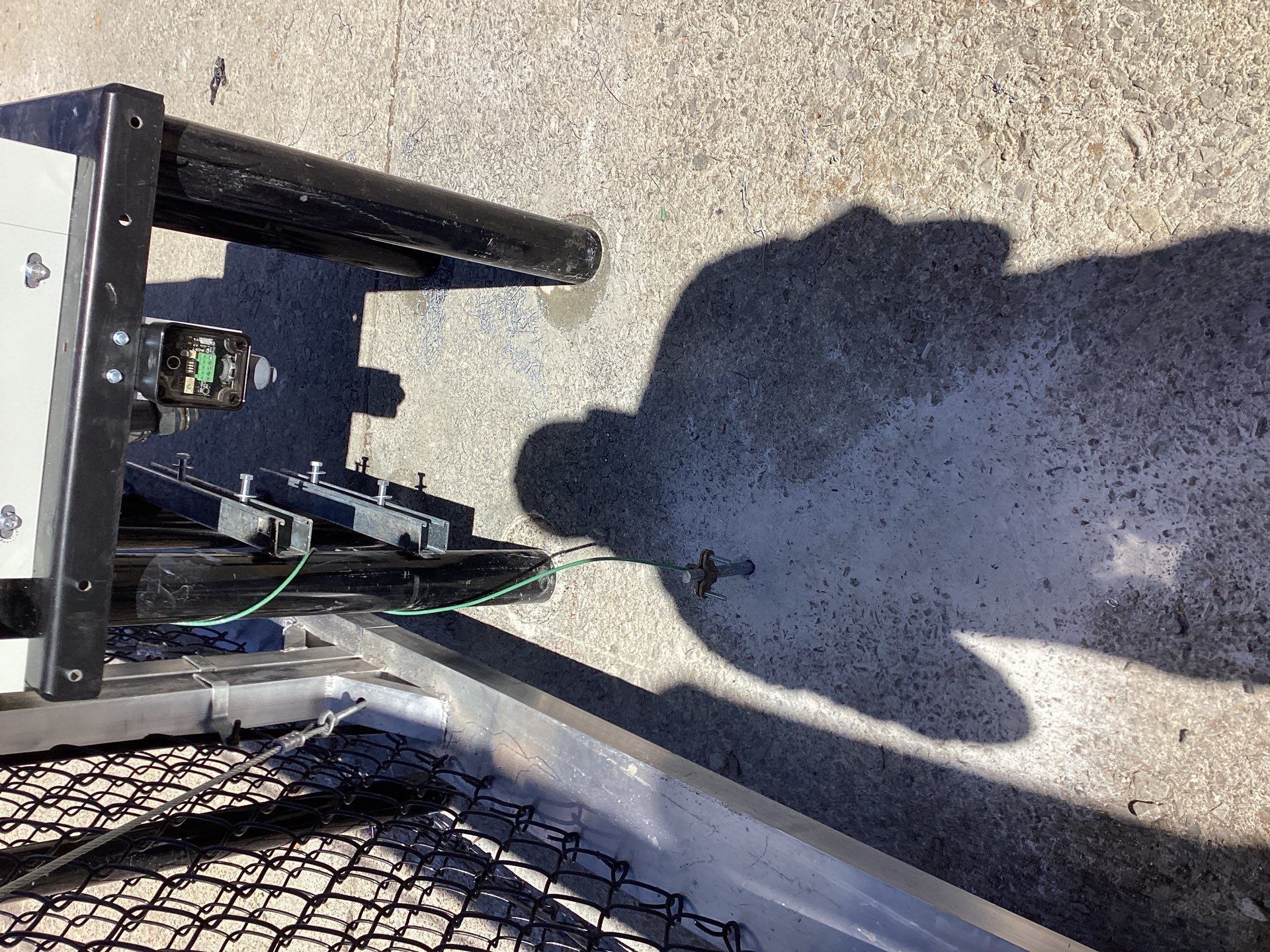 Shadow of a person on concrete near a metal cart with wires and hardware.