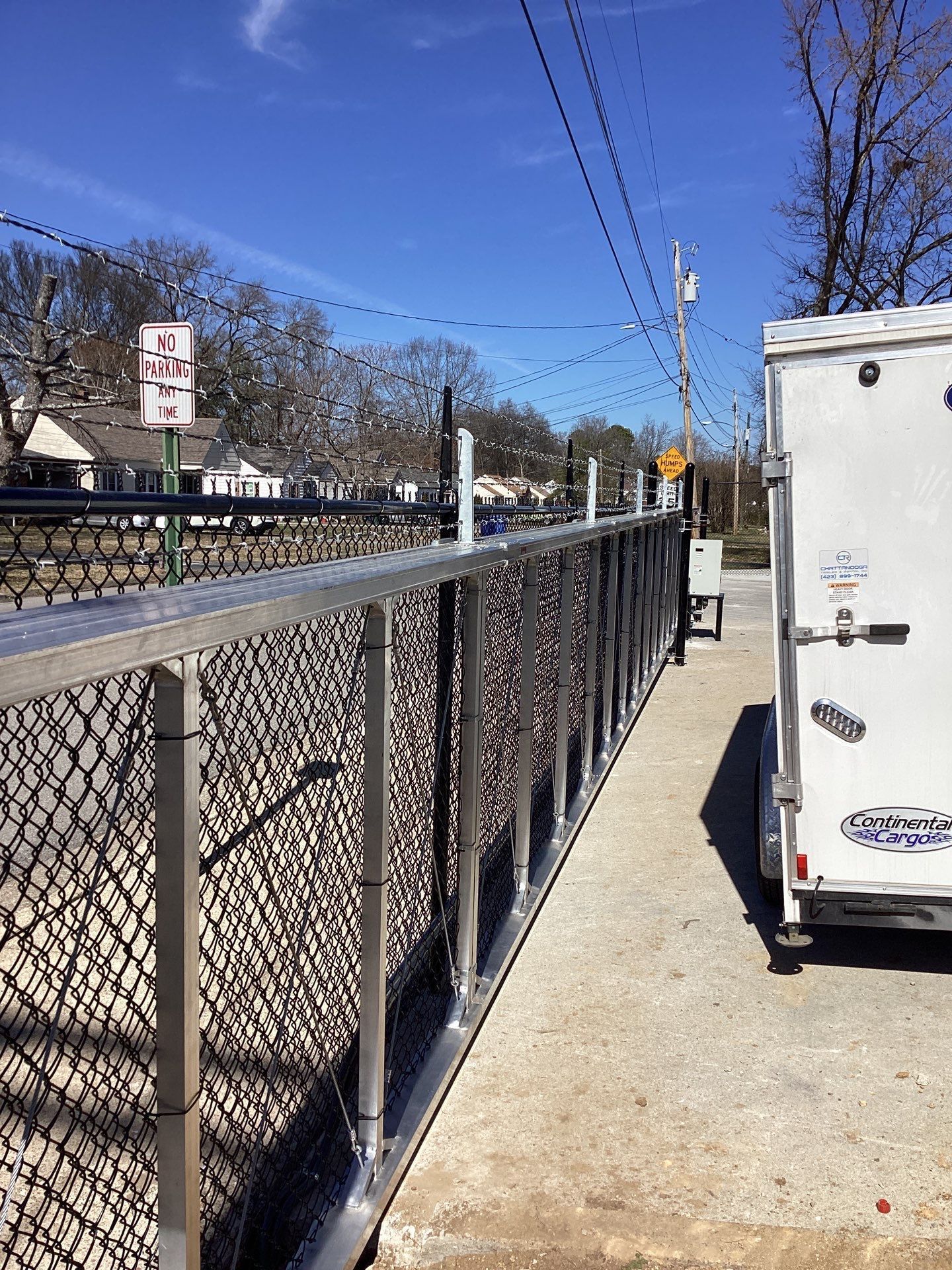 Chain-link fence with aluminum frame beside a white trailer on a sunny day.