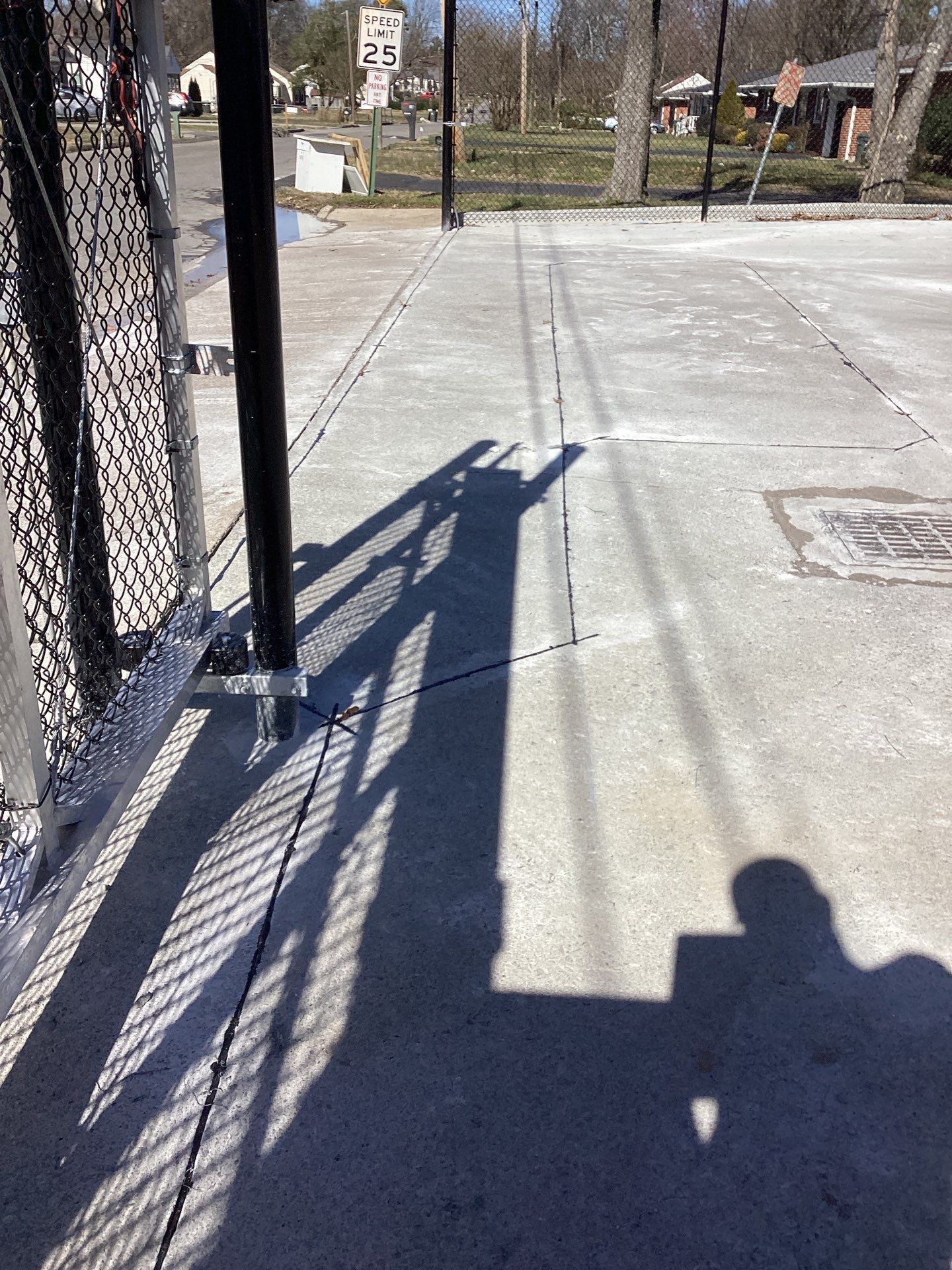 Shadows cast on a concrete path from a fence, pole, and sunlit day.