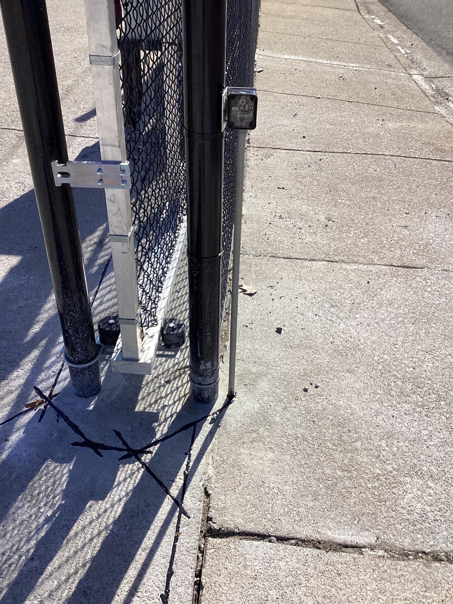 A chain-link fence gate on concrete; sunlight casts shadows.