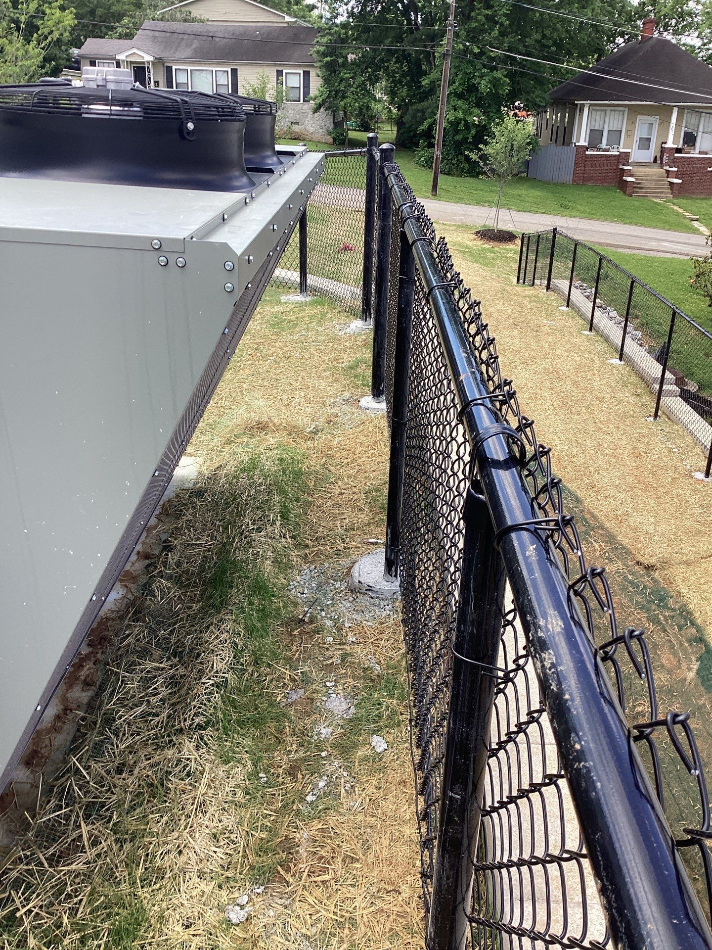 A black chain-link fence runs along a building's edge; short grass and a few houses are visible.