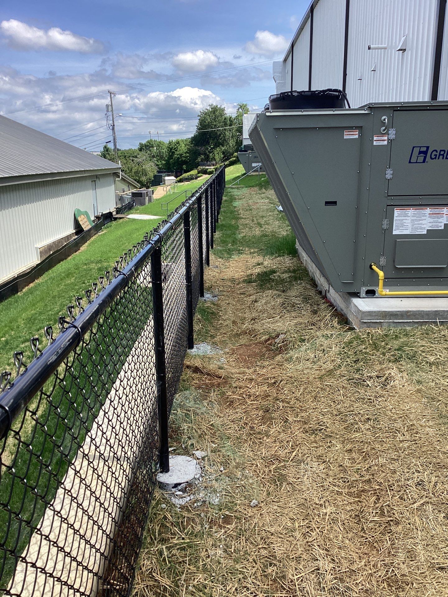 Black chain link fence along a grassy area next to industrial equipment.