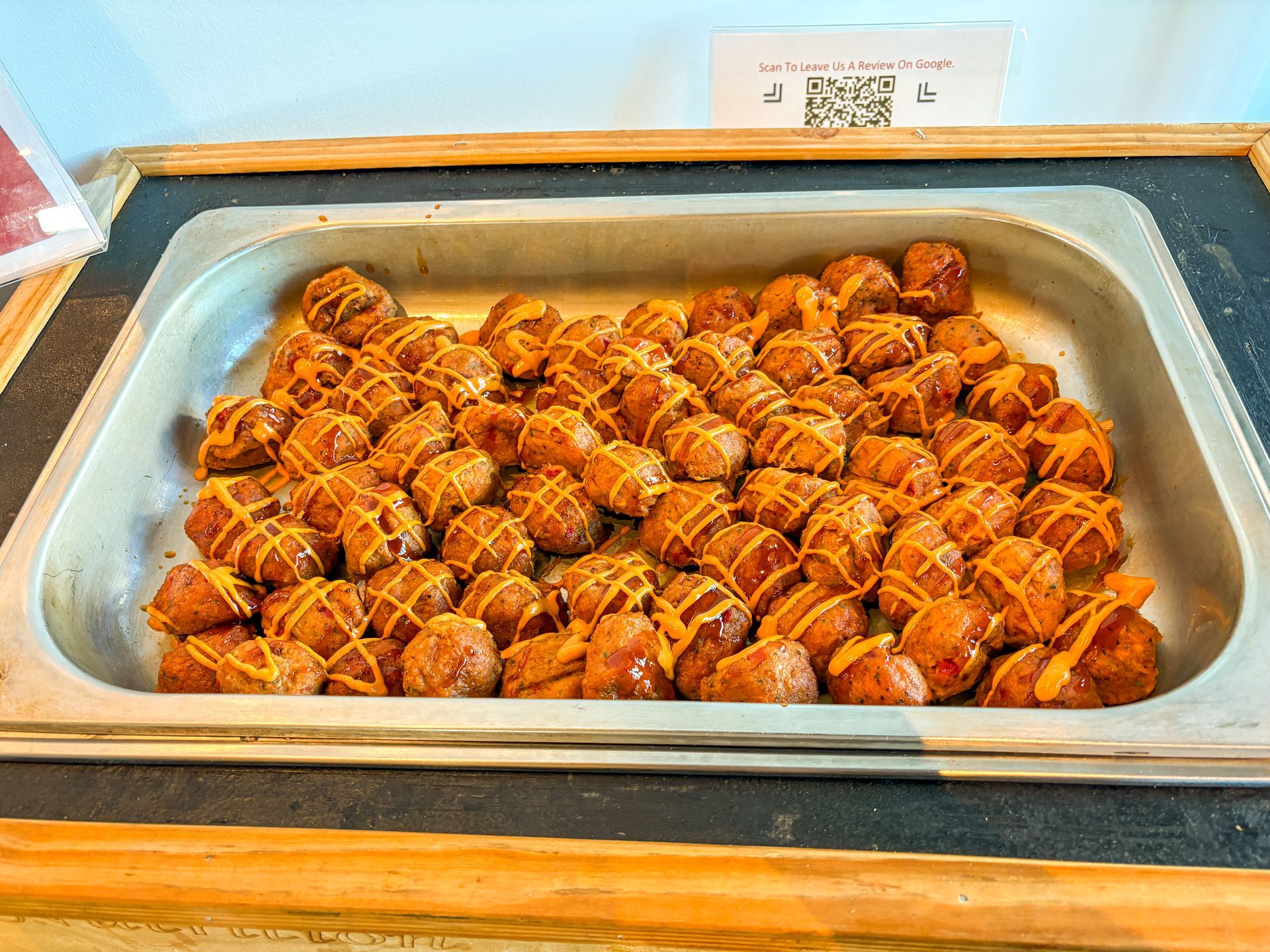 Tray of brown sausage balls drizzled with orange sauce.