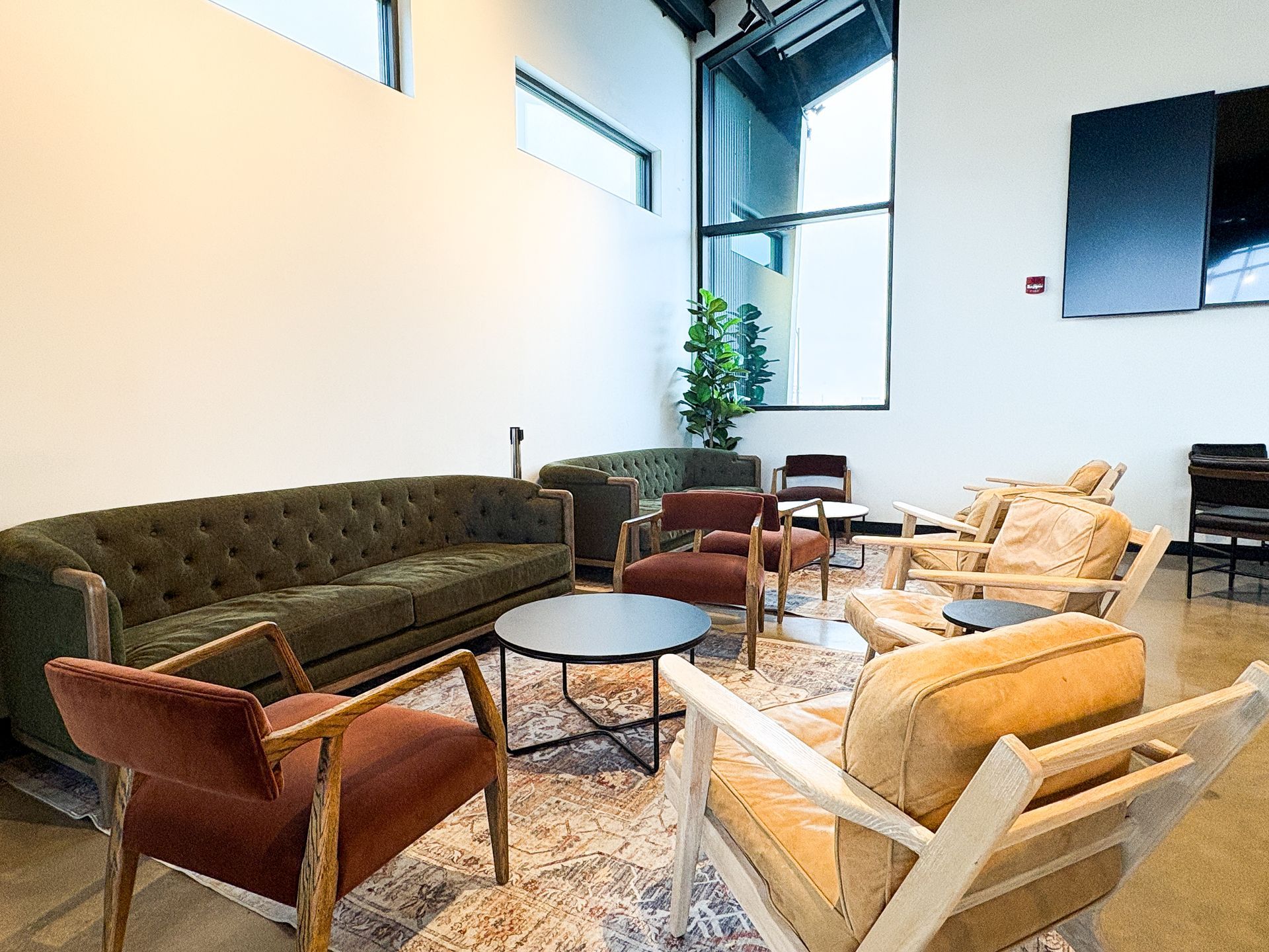 Lounge area with a dark green couch, armchairs, small tables, and a patterned rug.