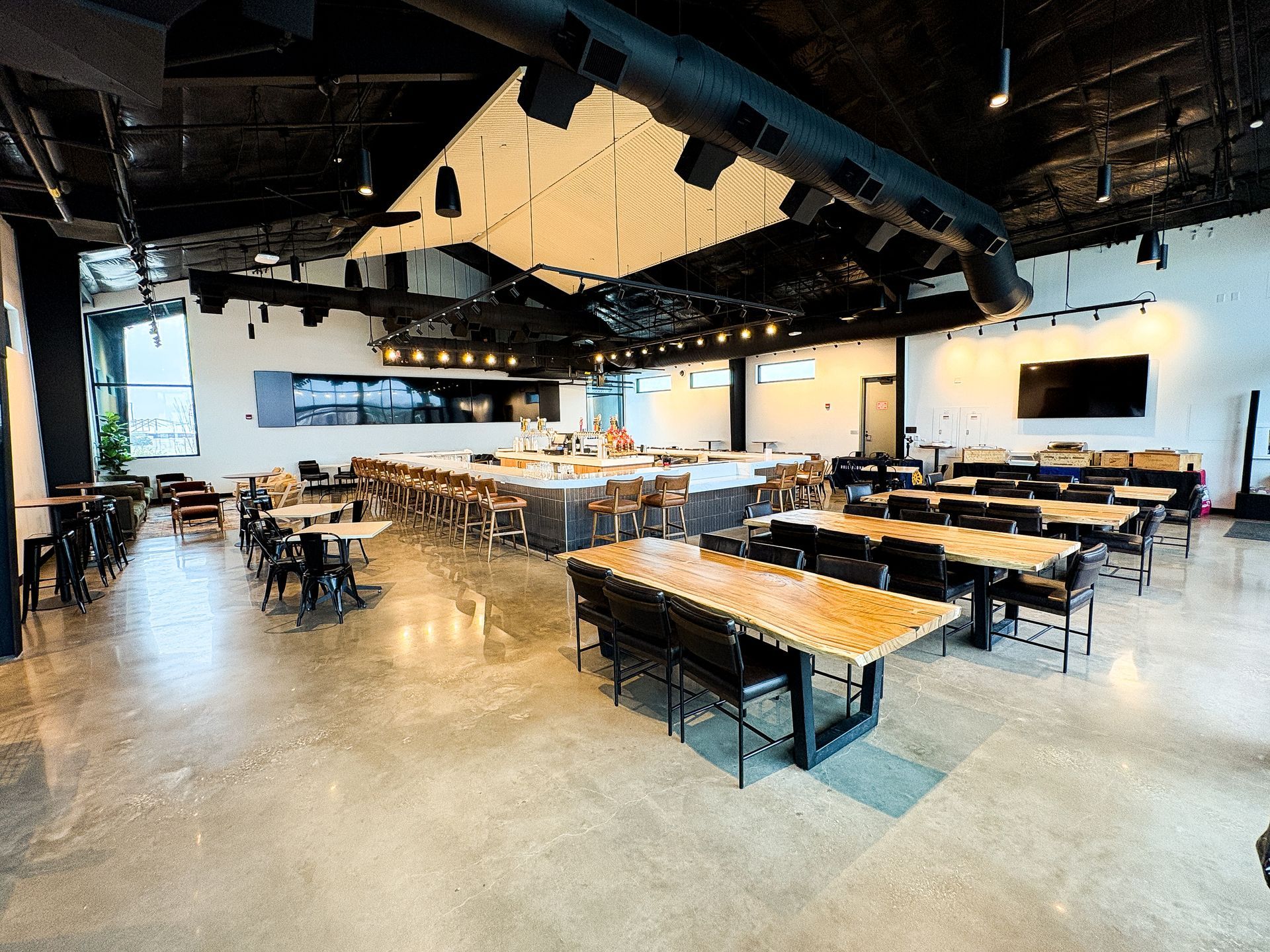 Interior of a modern restaurant with tables, chairs, bar, and exposed ceiling fixtures.