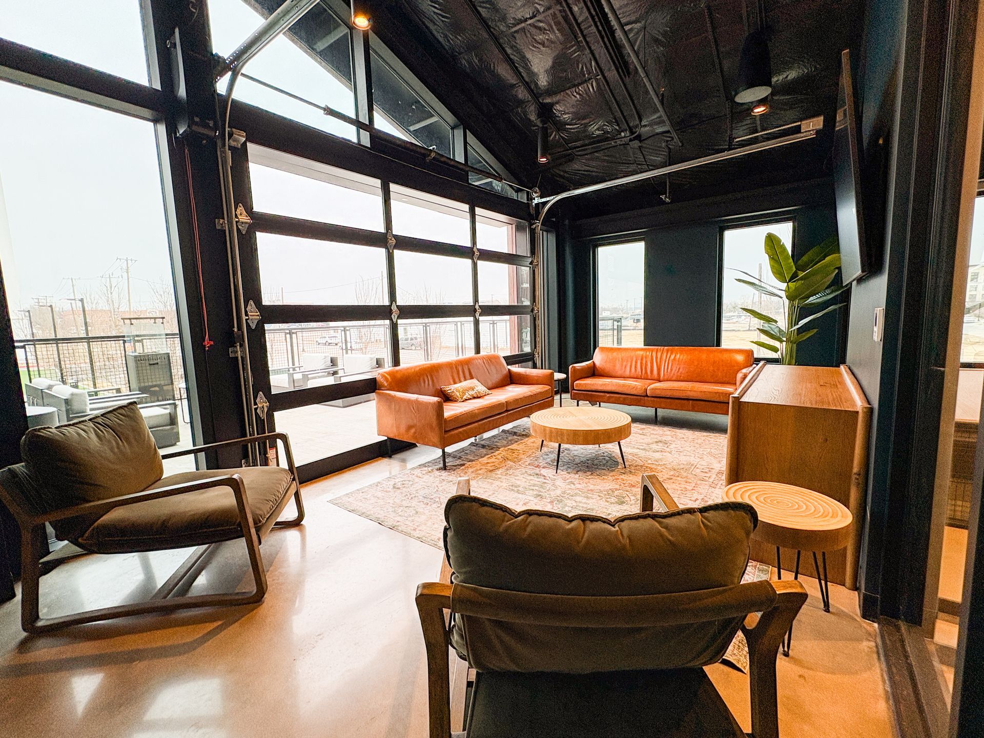 Modern lounge with leather sofas, chairs, and round coffee table. Large windows reveal an outdoor view.