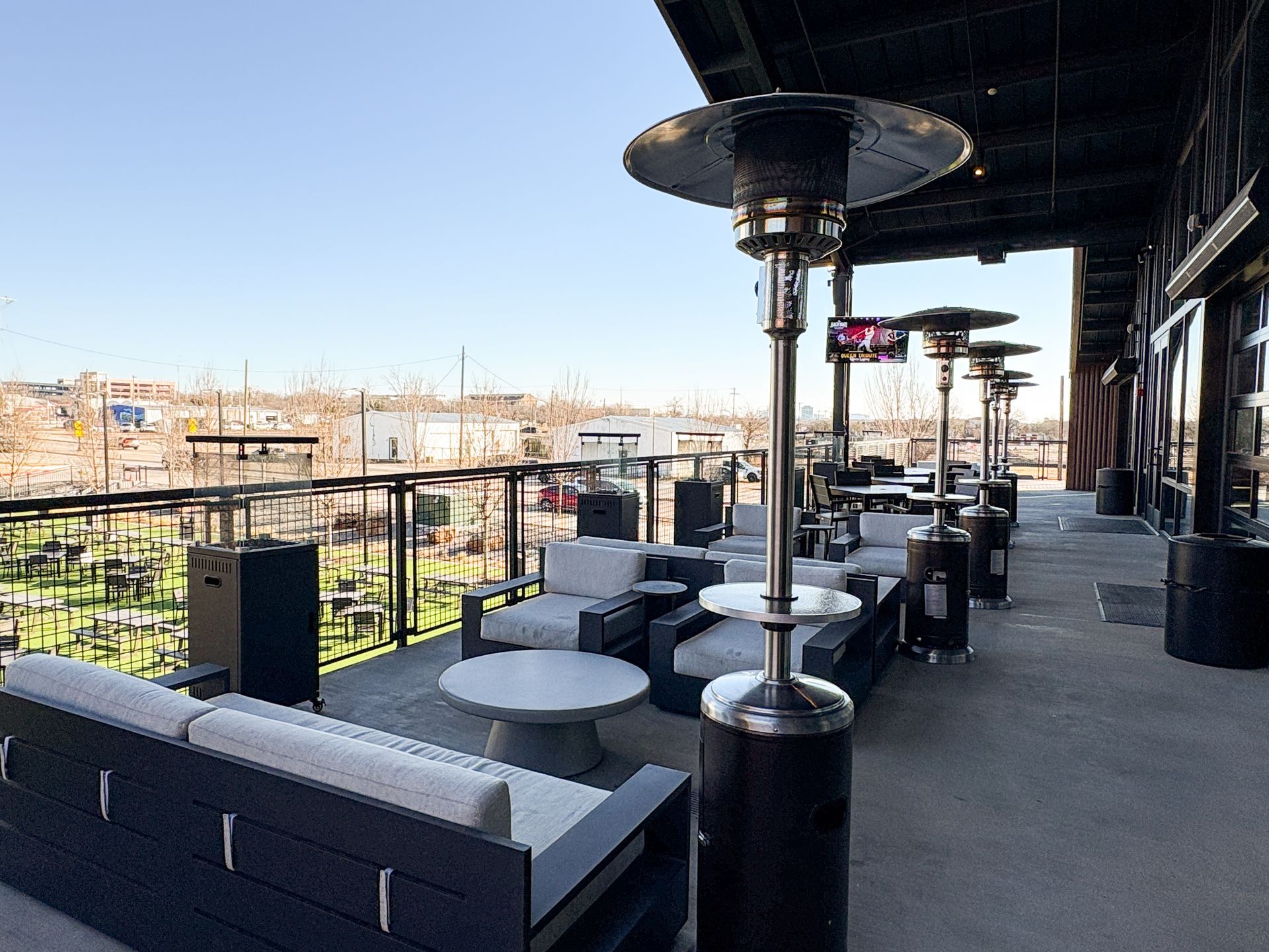 Outdoor patio with heaters, couches, tables, and city view.