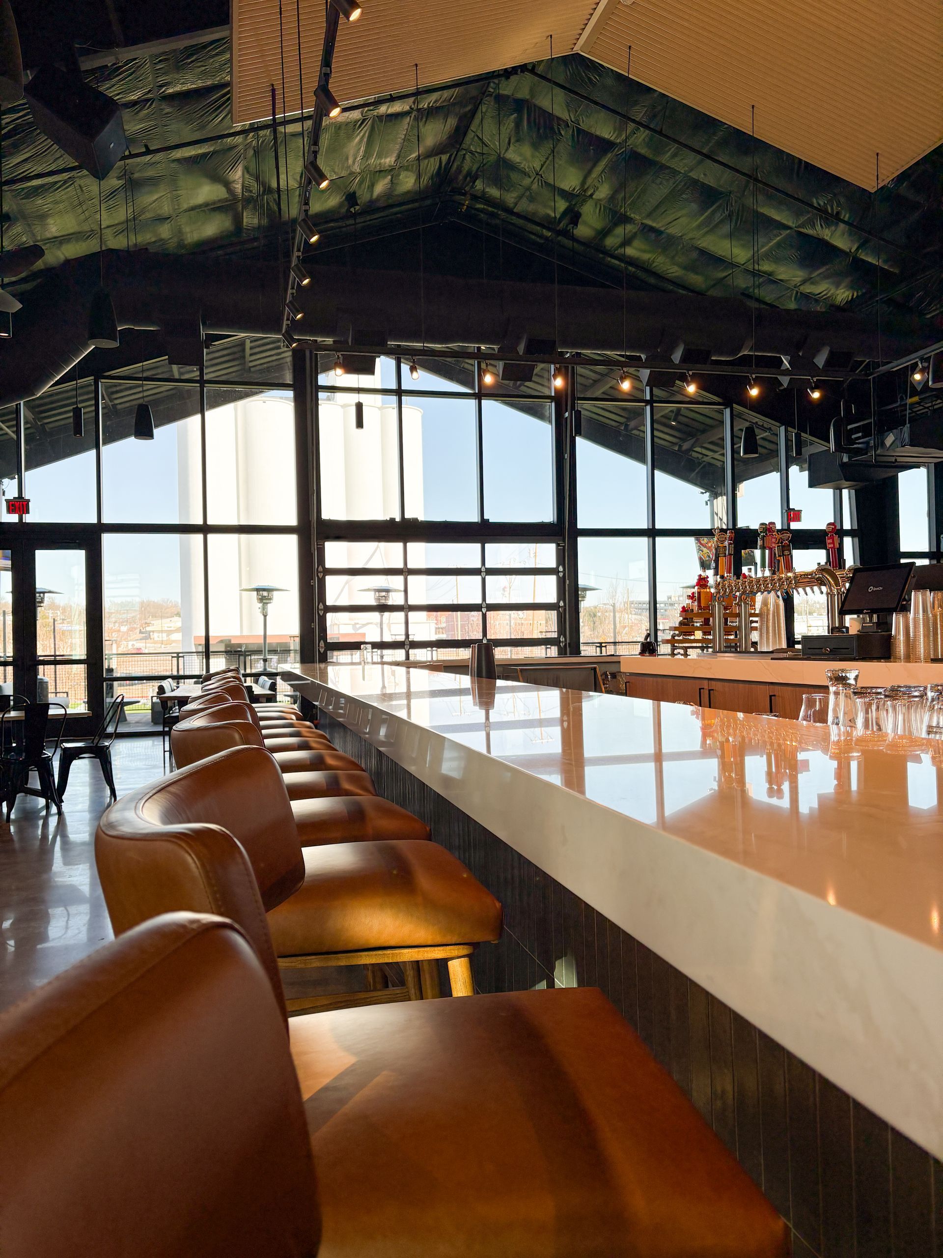 Empty bar with brown leather stools, overlooking a city skyline through large windows.