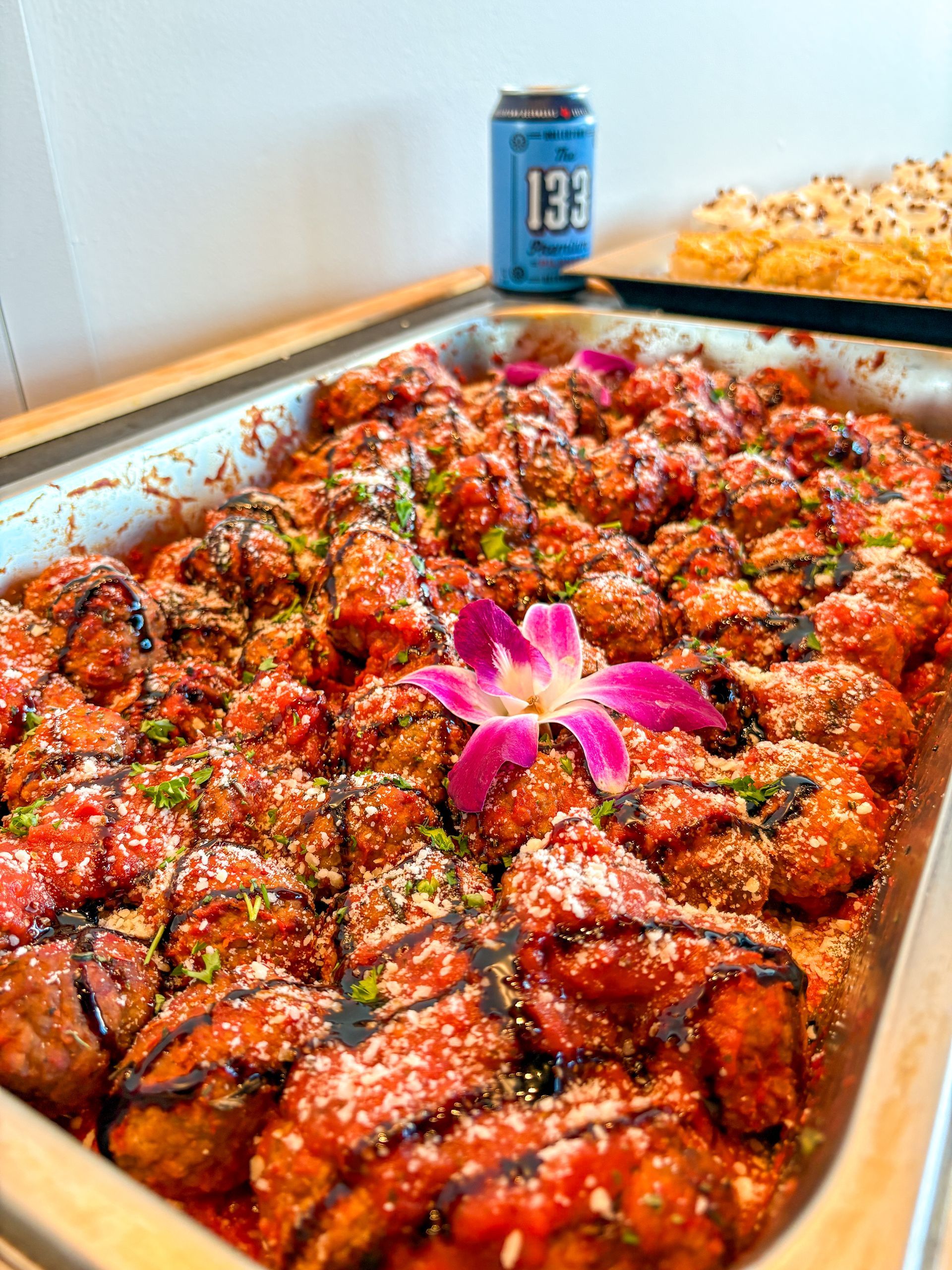Meatballs in red sauce topped with cheese, balsamic glaze, and a purple flower.