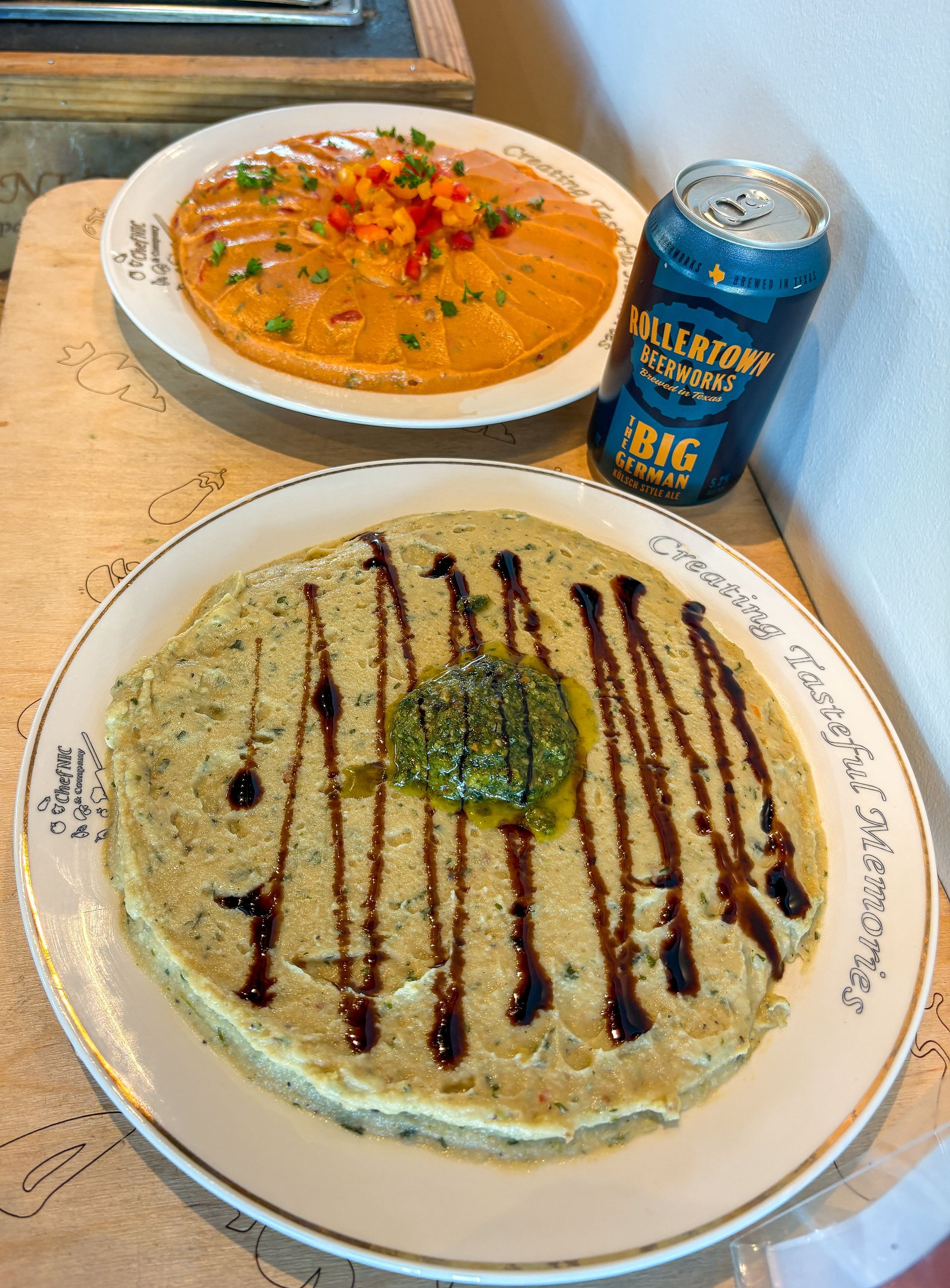 Two plates of food, one topped with sauce and shrimp, the other with pesto and balsamic glaze, next to a beer can.