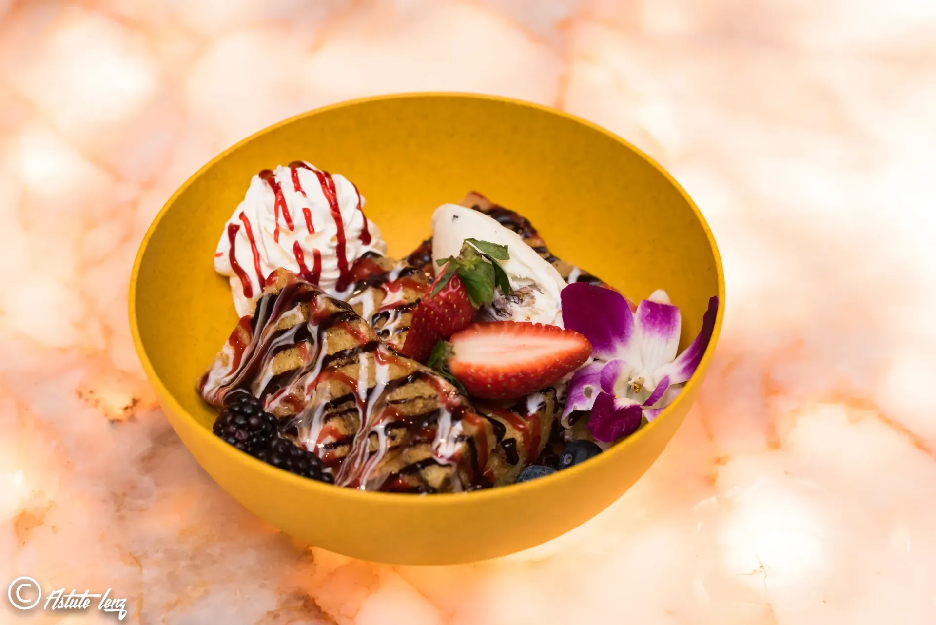 Dessert bowl with grilled dessert, berries, ice cream, and a flower.
