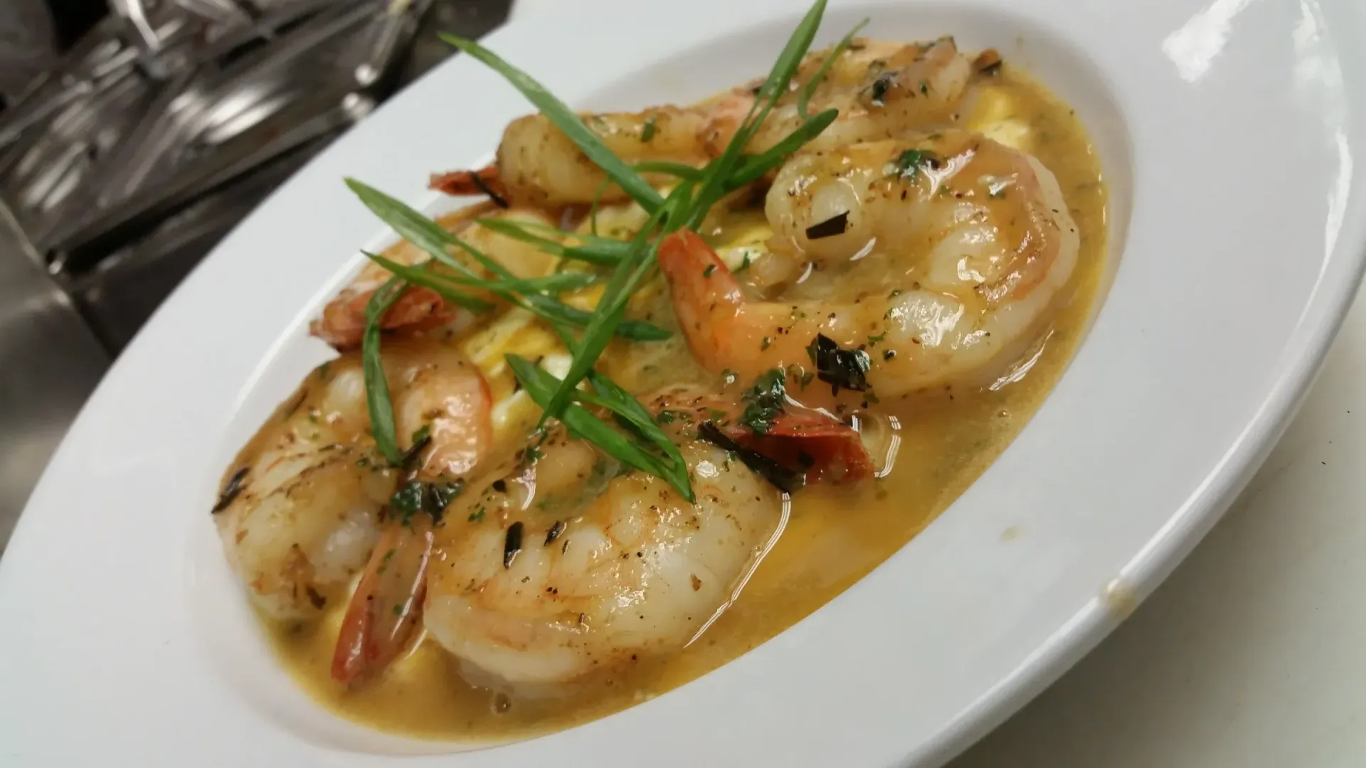 Shrimp scampi over grits, garnished with green onion, in a white oval dish.