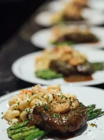 Plated steak dishes with shrimp, asparagus, and pasta in a row.