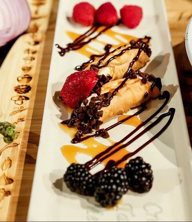 Cannoli dessert on a rectangular plate with caramel and chocolate drizzle, berries, and chocolate chips.