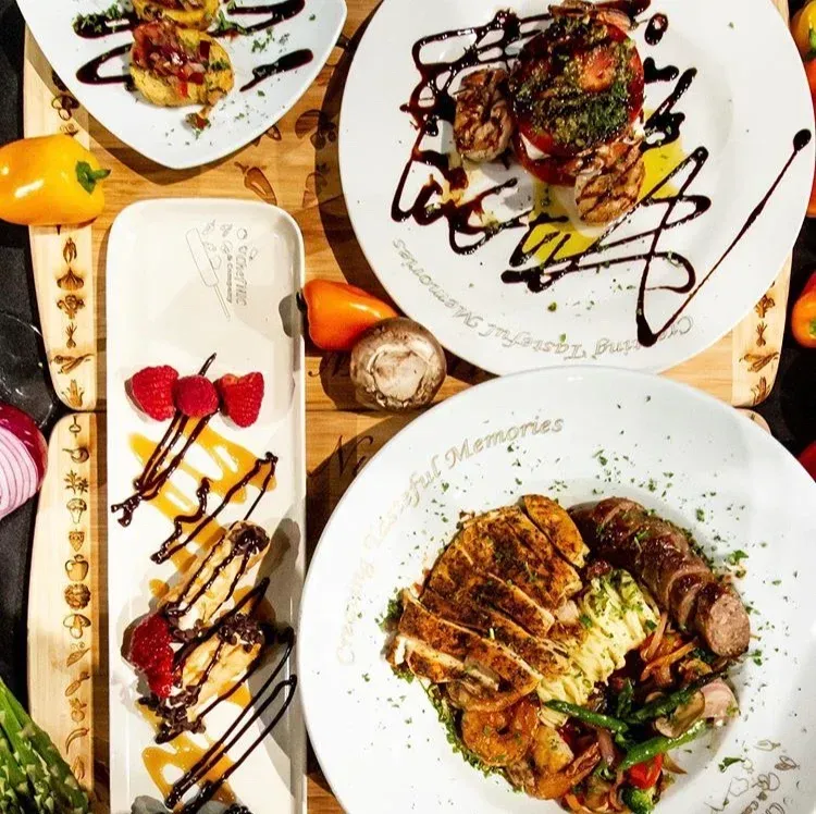 Overhead view of several plates of food, with grilled meat and vegetables; white plates with cursive text.