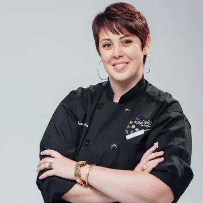 Woman in black chef's coat with arms crossed, smiling.