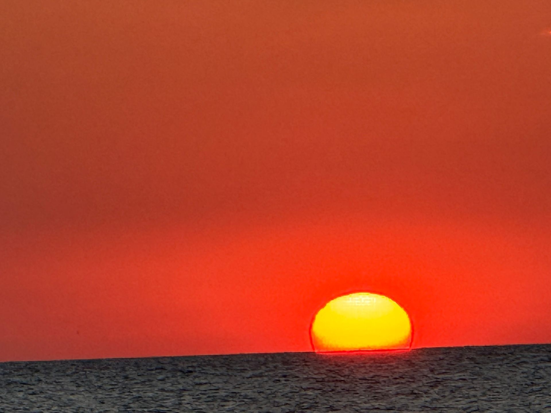 Vibrant orange sunset over dark ocean horizon; the sun is a bright yellow orb.
