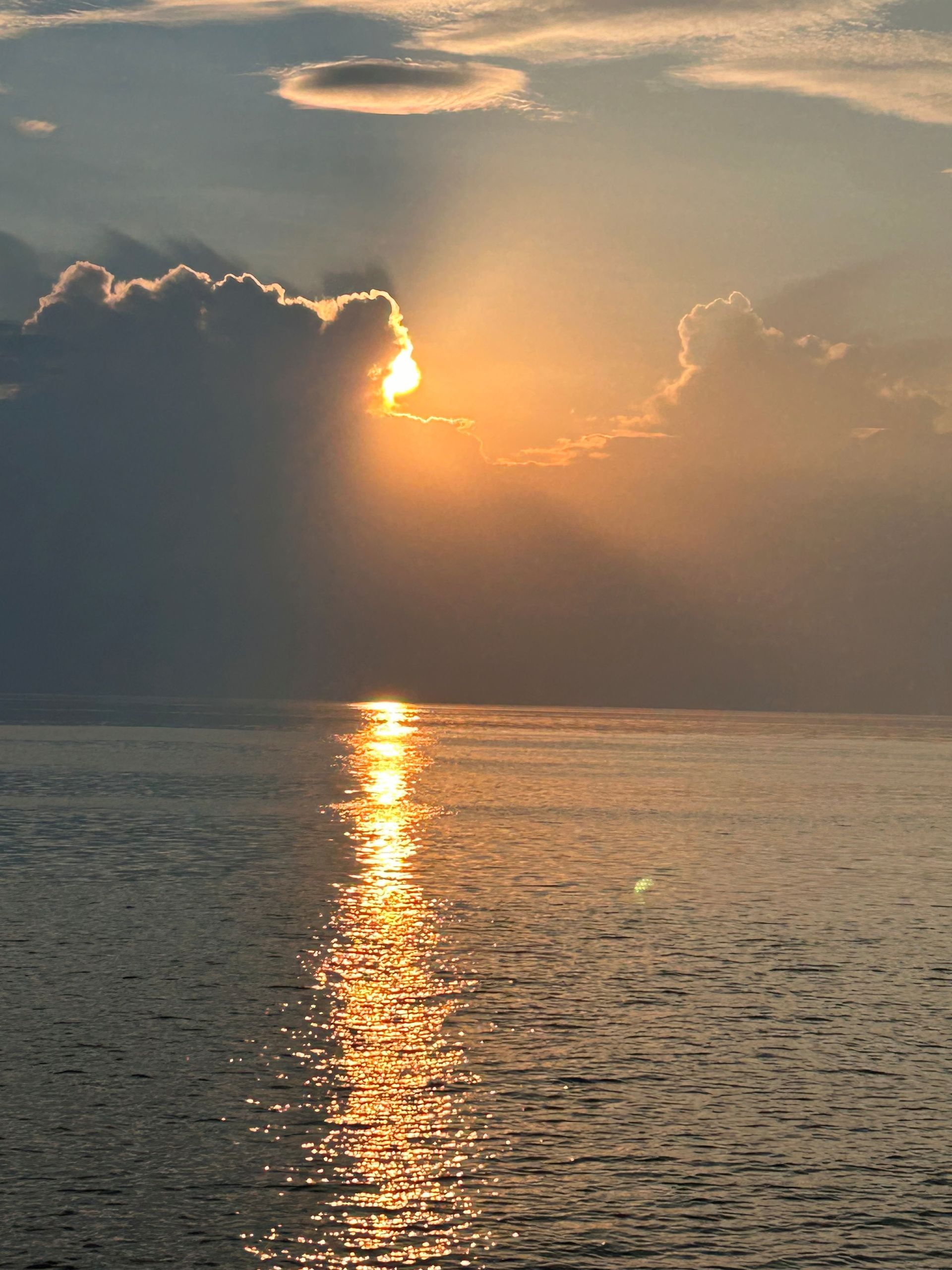 Sunset over ocean, sun breaking through clouds, reflecting light on water.