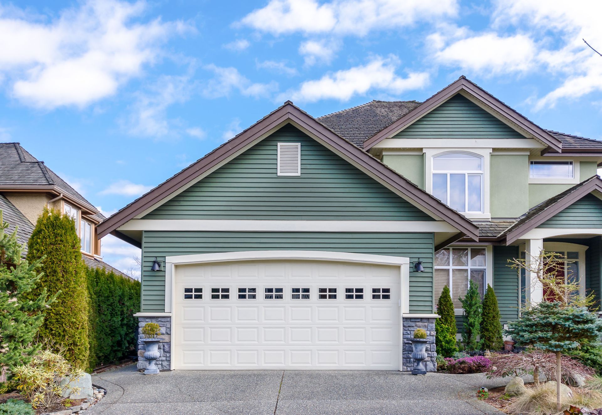 Green house with a white garage door, blue sky.