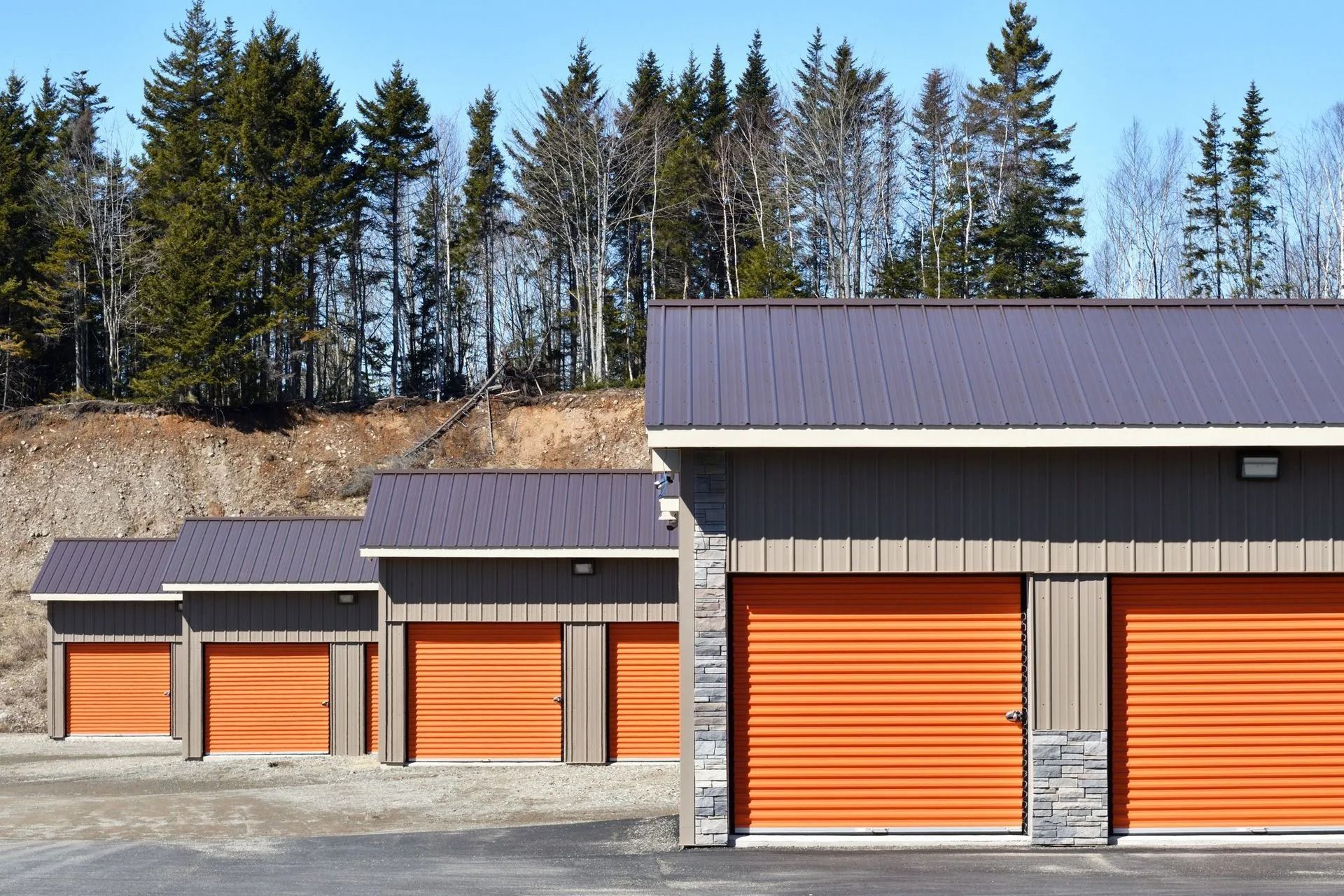 Row of orange storage unit doors with gray roofs and siding, in front of a forest.
