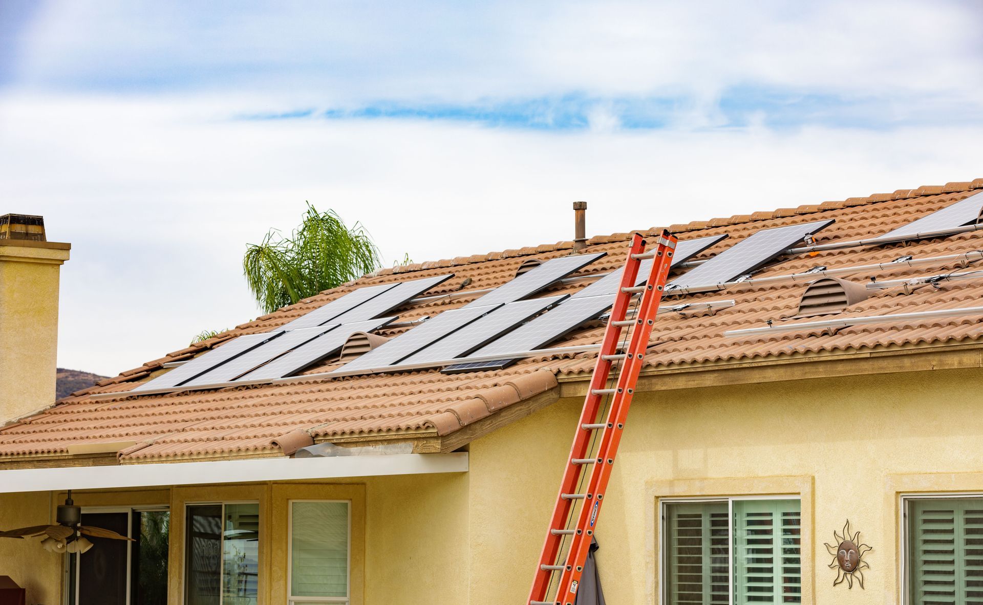 A ladder leaning against a house roof with solar panels installed.