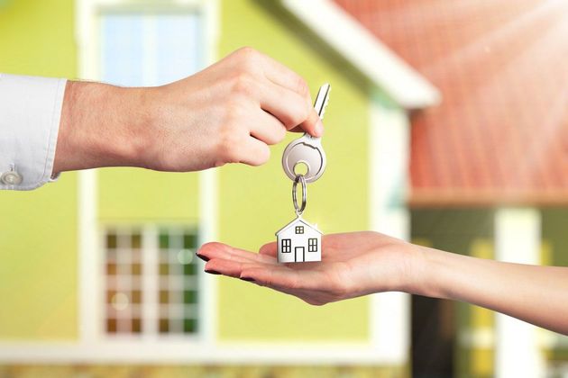 Person handing house key to another person, in front of a house.