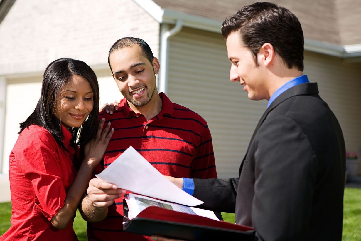Three people reviewing documents together outdoors, smiling and pointing at papers.