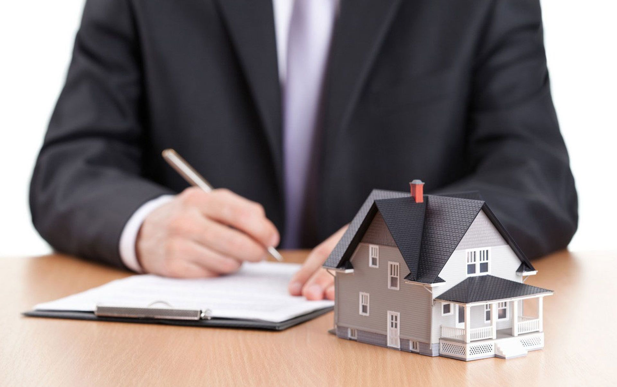Businessperson writing beside a model house on a desk