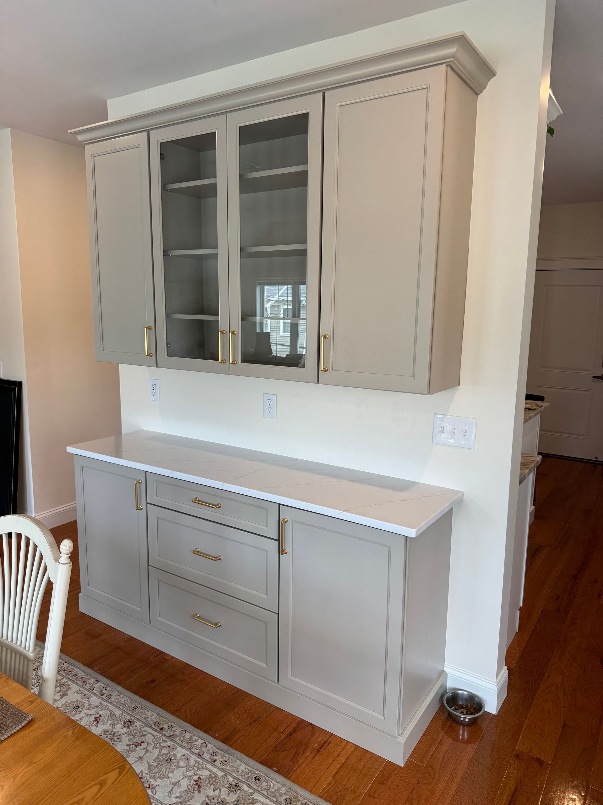 Beige built-in kitchen cabinet with glass-front upper doors and white countertop against a wall.