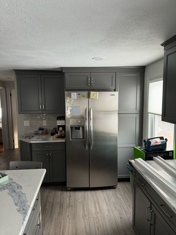 A modern kitchen with dark grey cabinets, a stainless steel side-by-side refrigerator, and a light-colored countertop.
