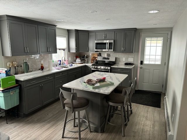 A modern kitchen with dark gray cabinets, a white marble-topped island with stools, and a door leading outside.