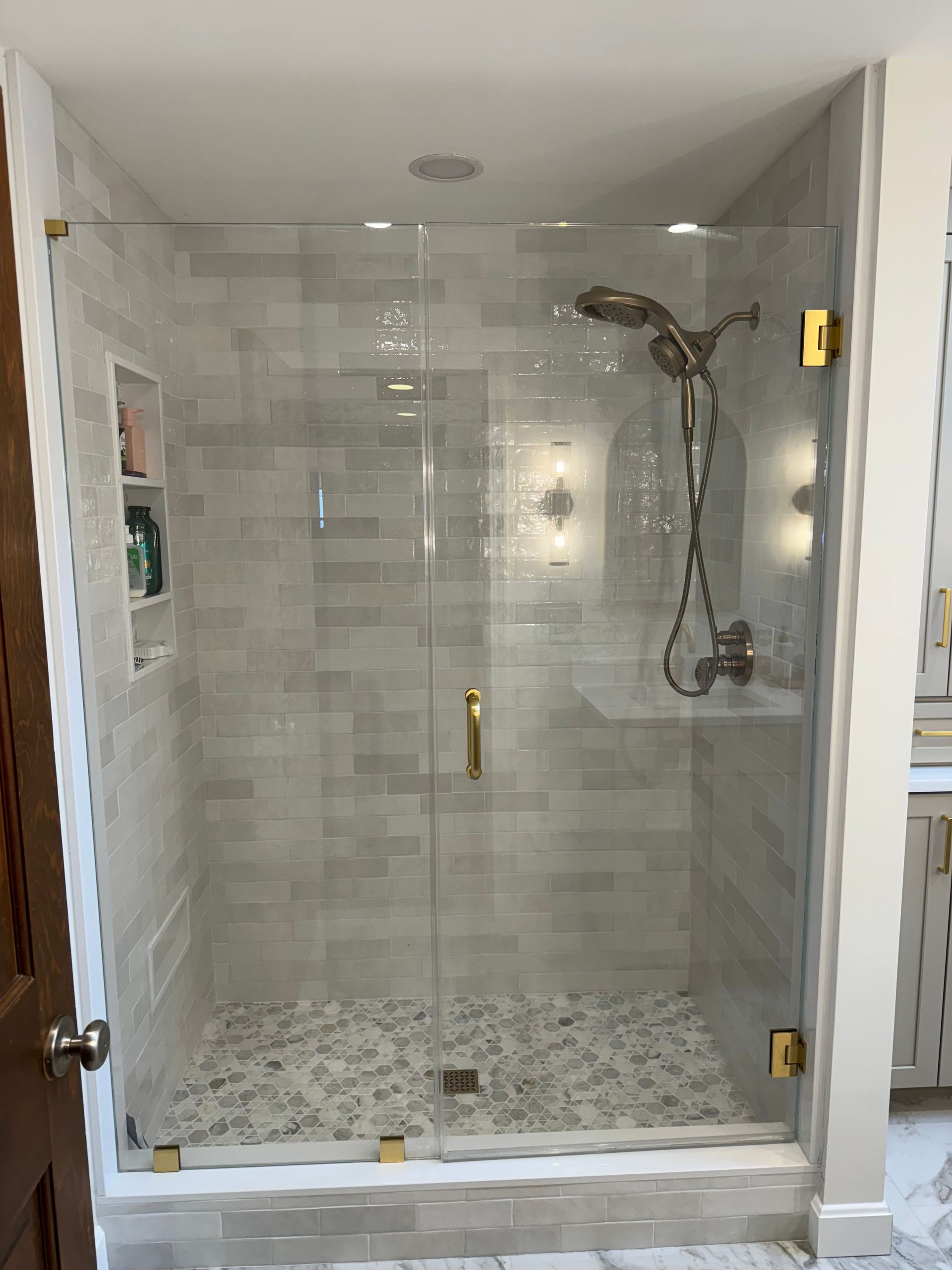 Glass-tiled walk-in shower with brass fixtures and pebble mosaic floor