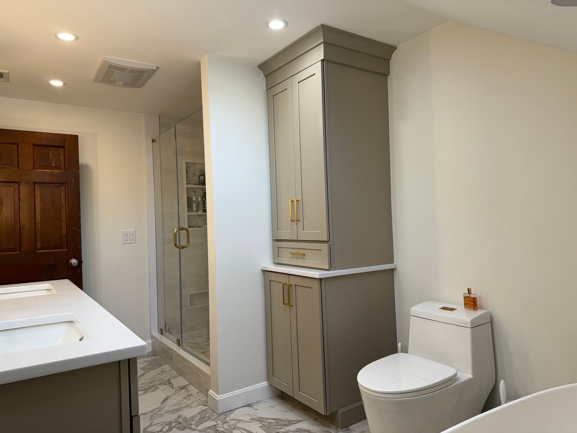Bathroom with white vanity, toilet, beige cabinet, and tiled shower in a bright, modern interior