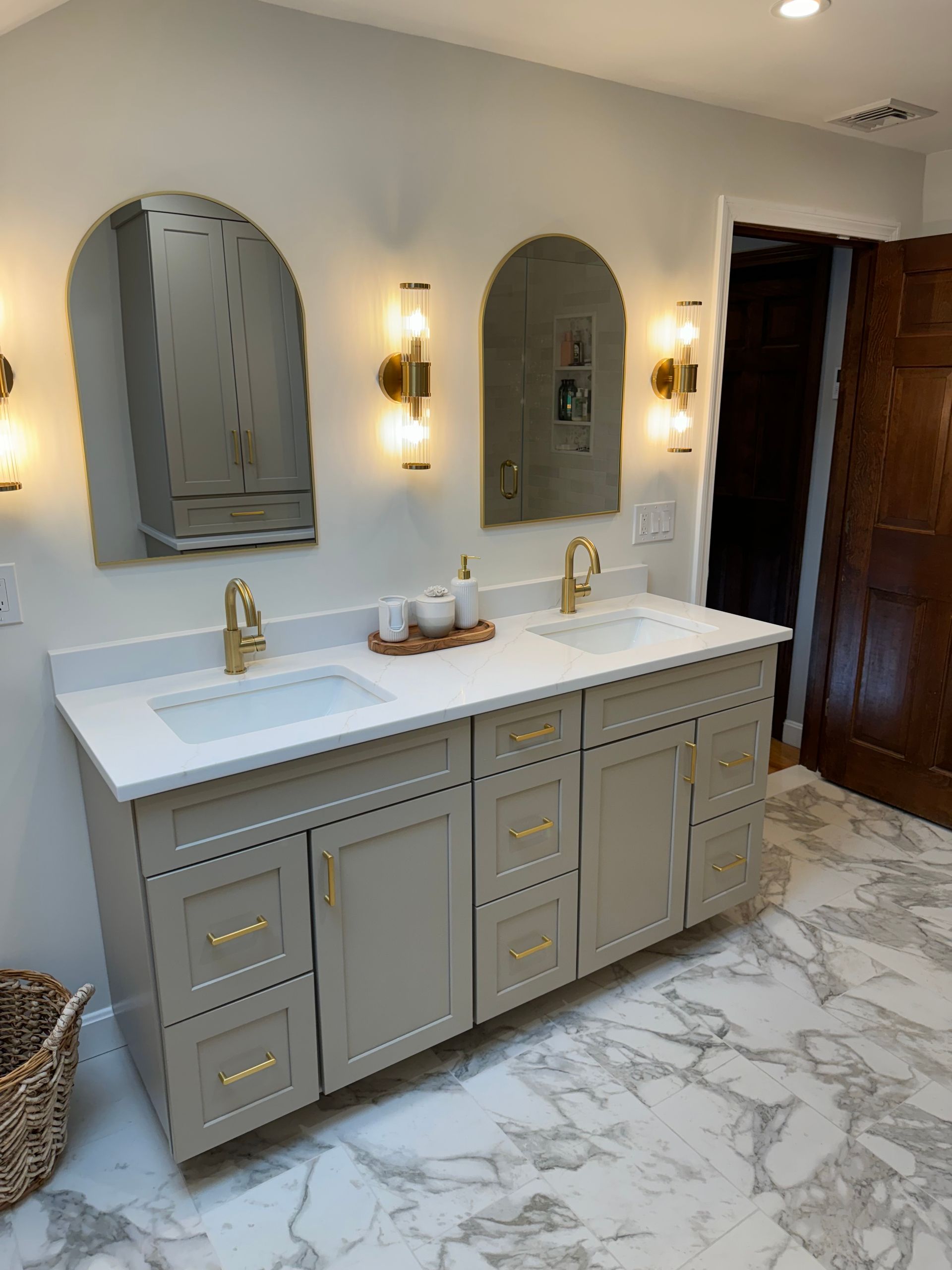 Elegant double vanity bathroom with arched mirrors, brass sconces, and light marble floor tiles