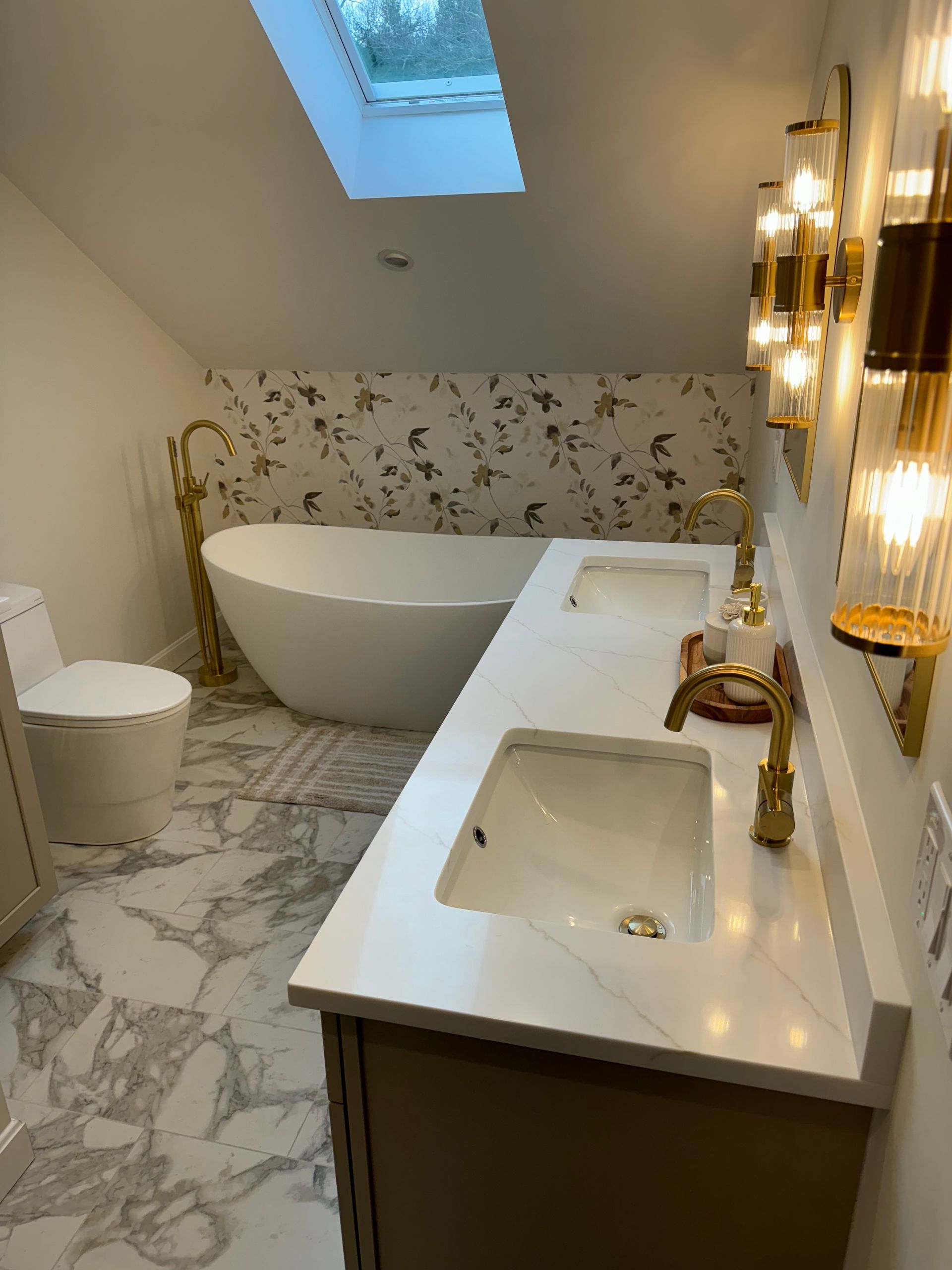 Modern bathroom with freestanding tub, marble vanity, skylight, and floral wallpaper