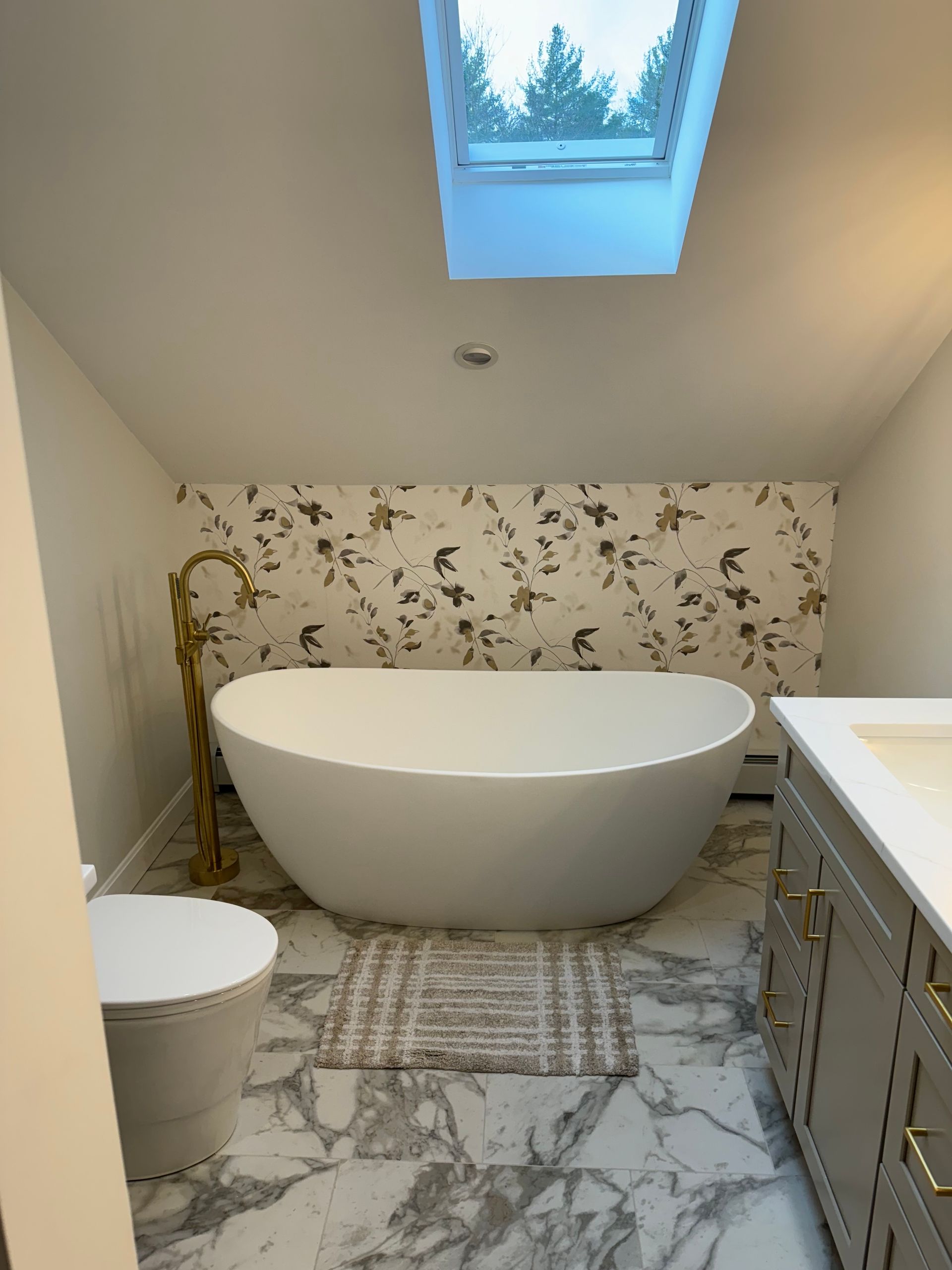 Modern bathroom with a freestanding tub, skylight, marble floor, and floral accent wall