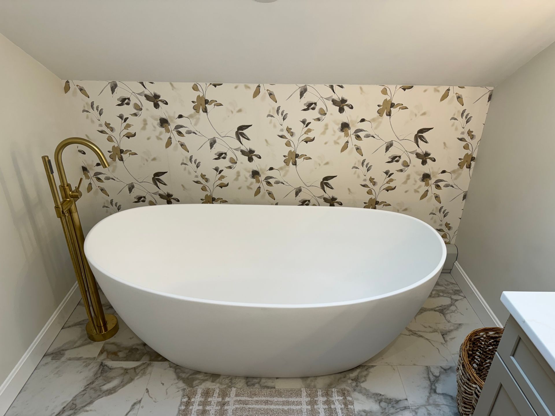 Modern freestanding white bathtub in a floral wallpapered bathroom nook