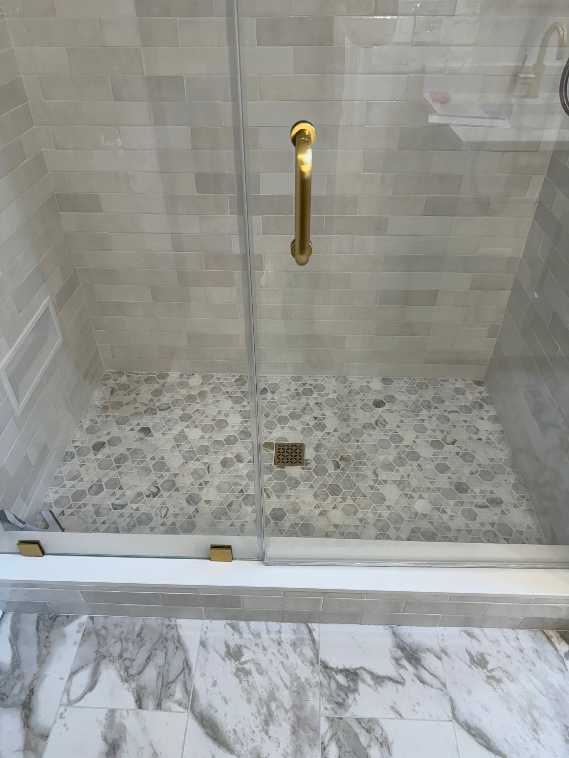 Walk-in shower with glass door, gold handle, and gray tile walls and floor.