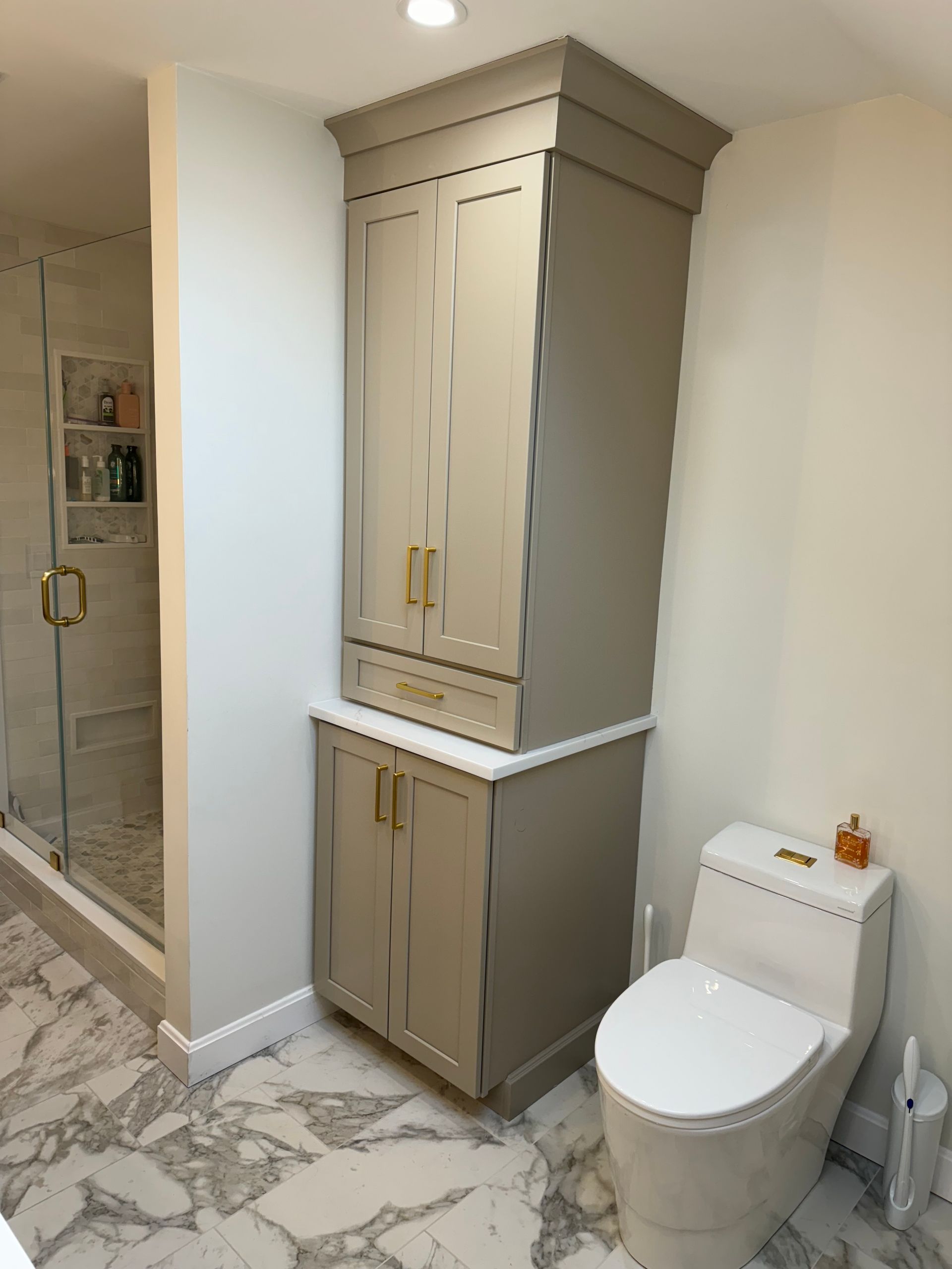 Bathroom with marble tile, a built-in cabinet over a lower vanity, and a toilet beside it.