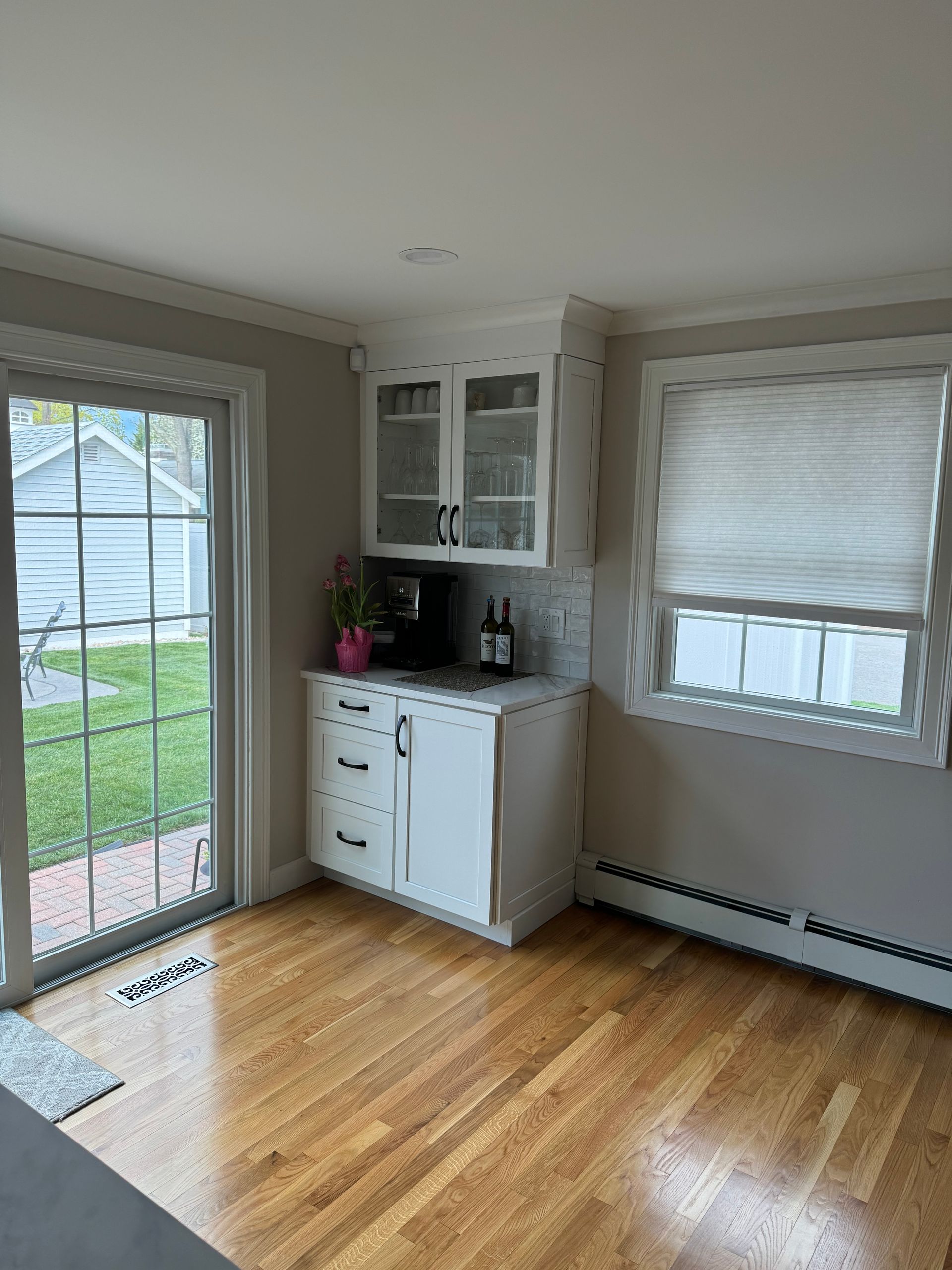Bright empty room with hardwood floors, white cabinet, bay window, and sliding glass door to a yard.