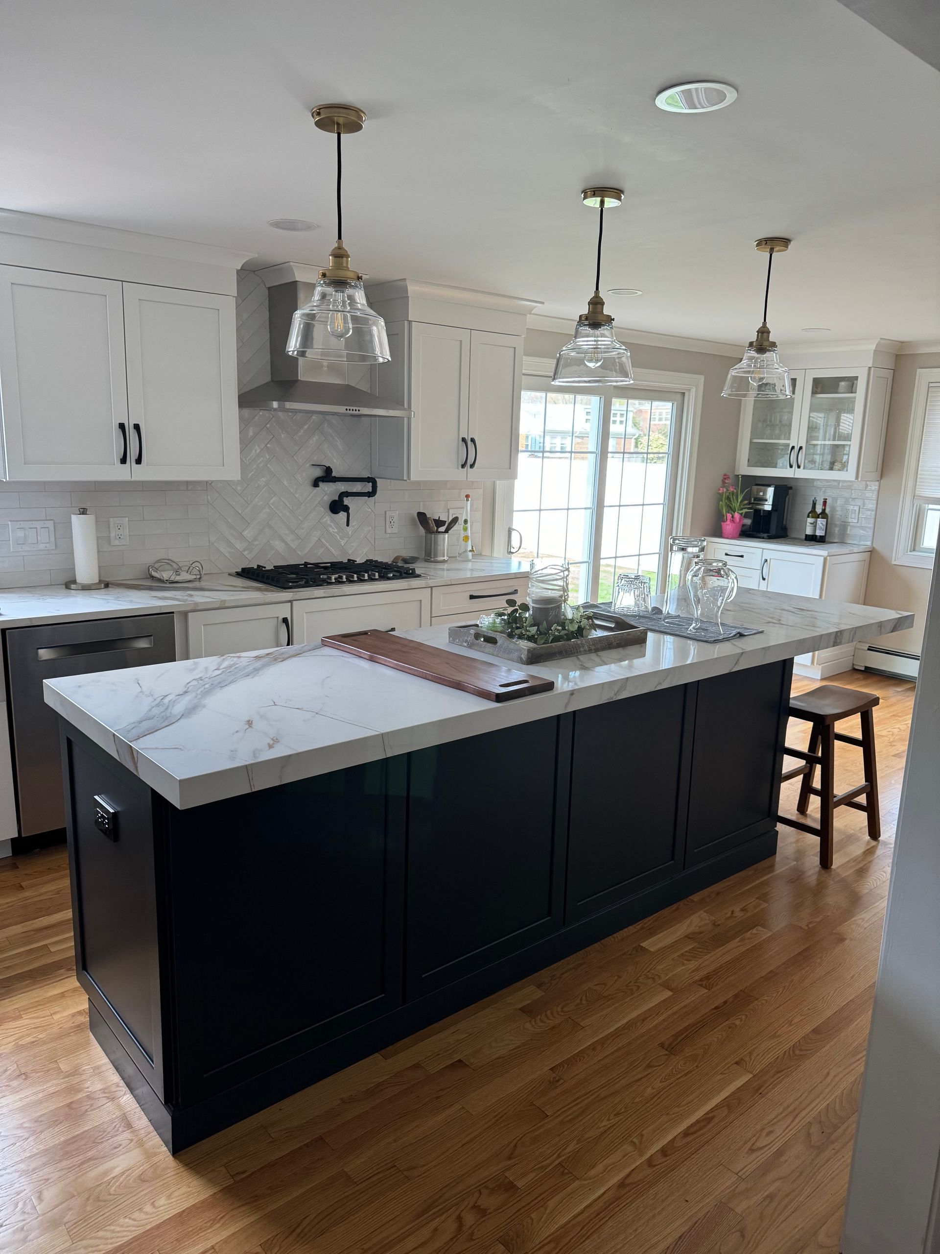 Modern kitchen with dark island, white cabinets, pendant lights, and hardwood floors