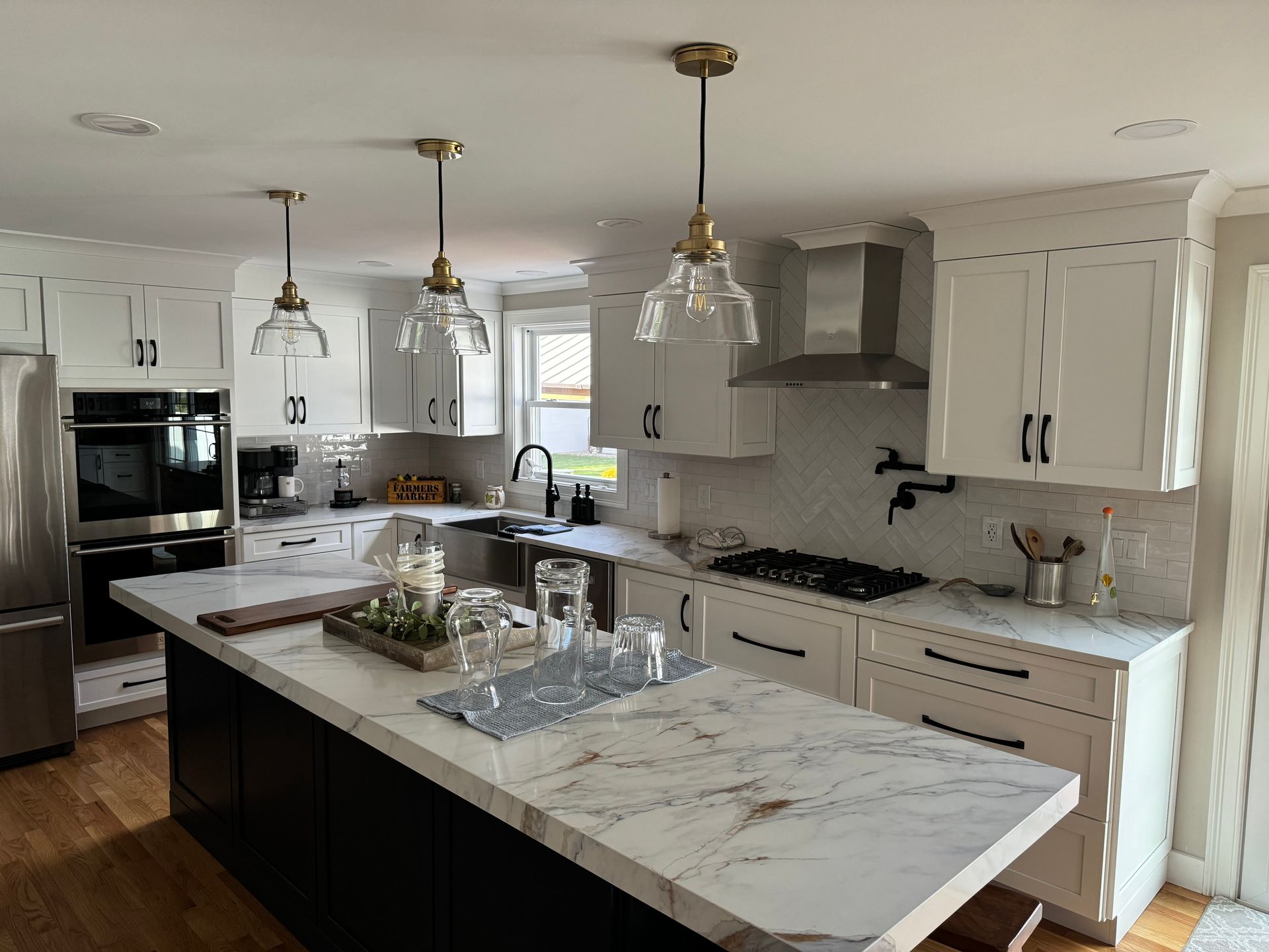 Bright modern kitchen with white cabinets, marble island, pendant lights, and stainless steel appliances