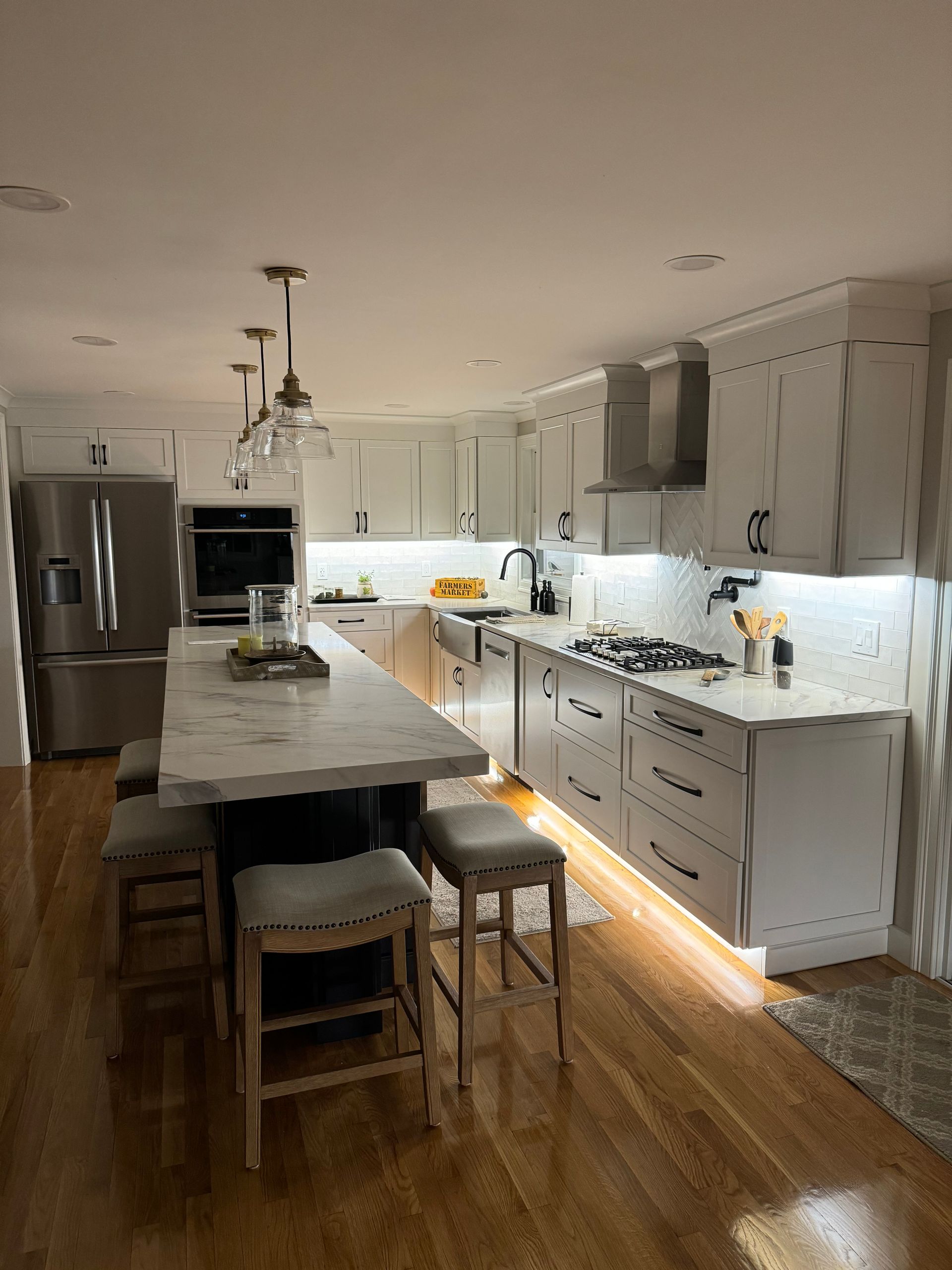 Modern white kitchen with island, pendant lights, stainless fridge, and sunlit wood floors